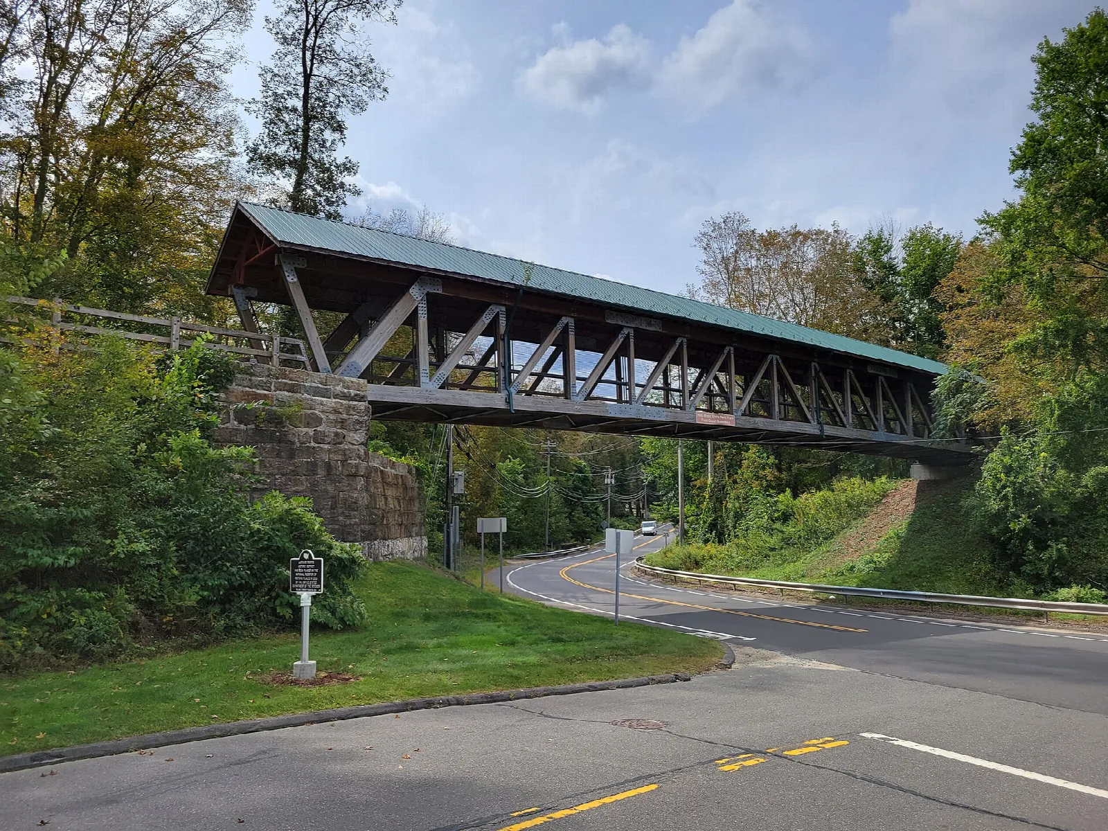 Covered footbridge arching over a road beside fall trees