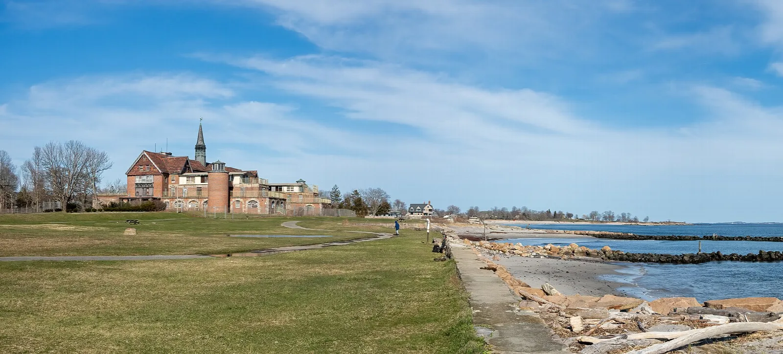 Grass lawn and rocky shoreline leading to a brick building in the distance