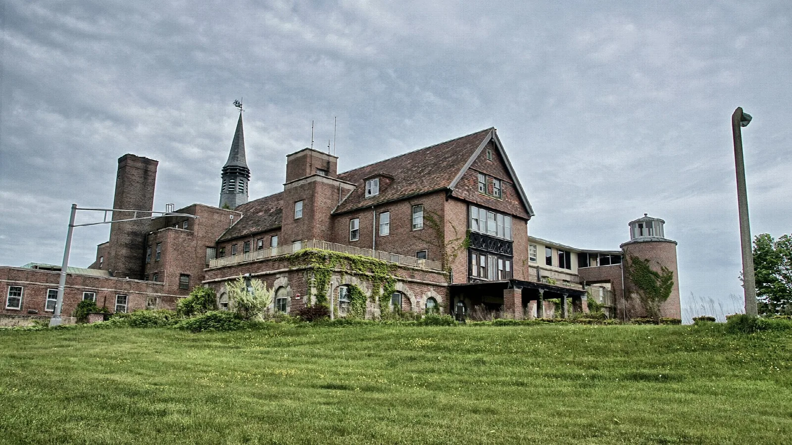 Brick building with chimneys and a spire above a green lawn