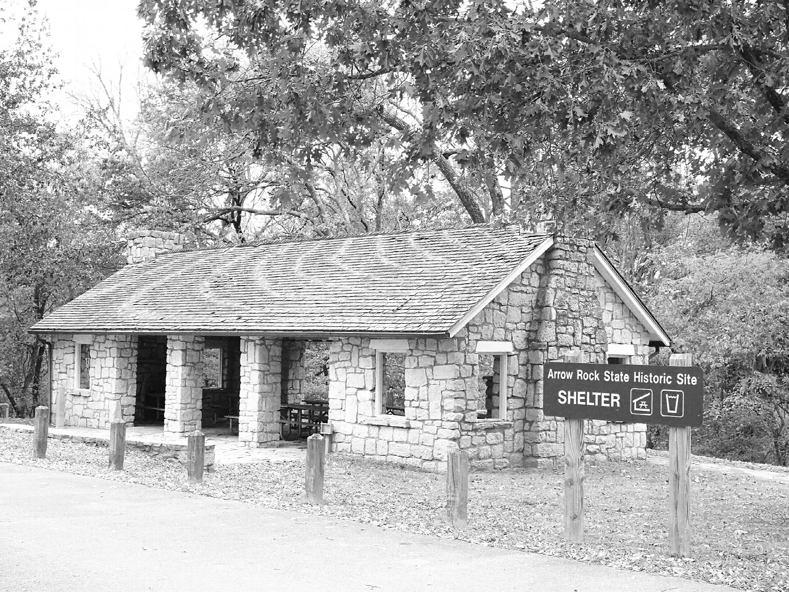 Black and white photo of a low stone shelter building among trees