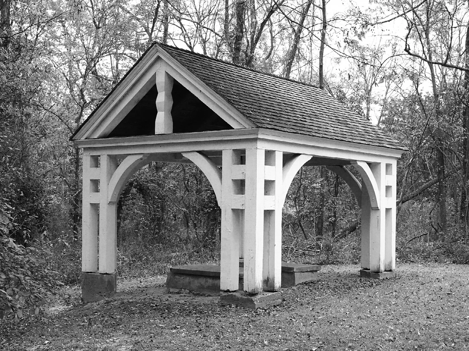 Black and white photo of a white open-sided wooden shelter in the woods