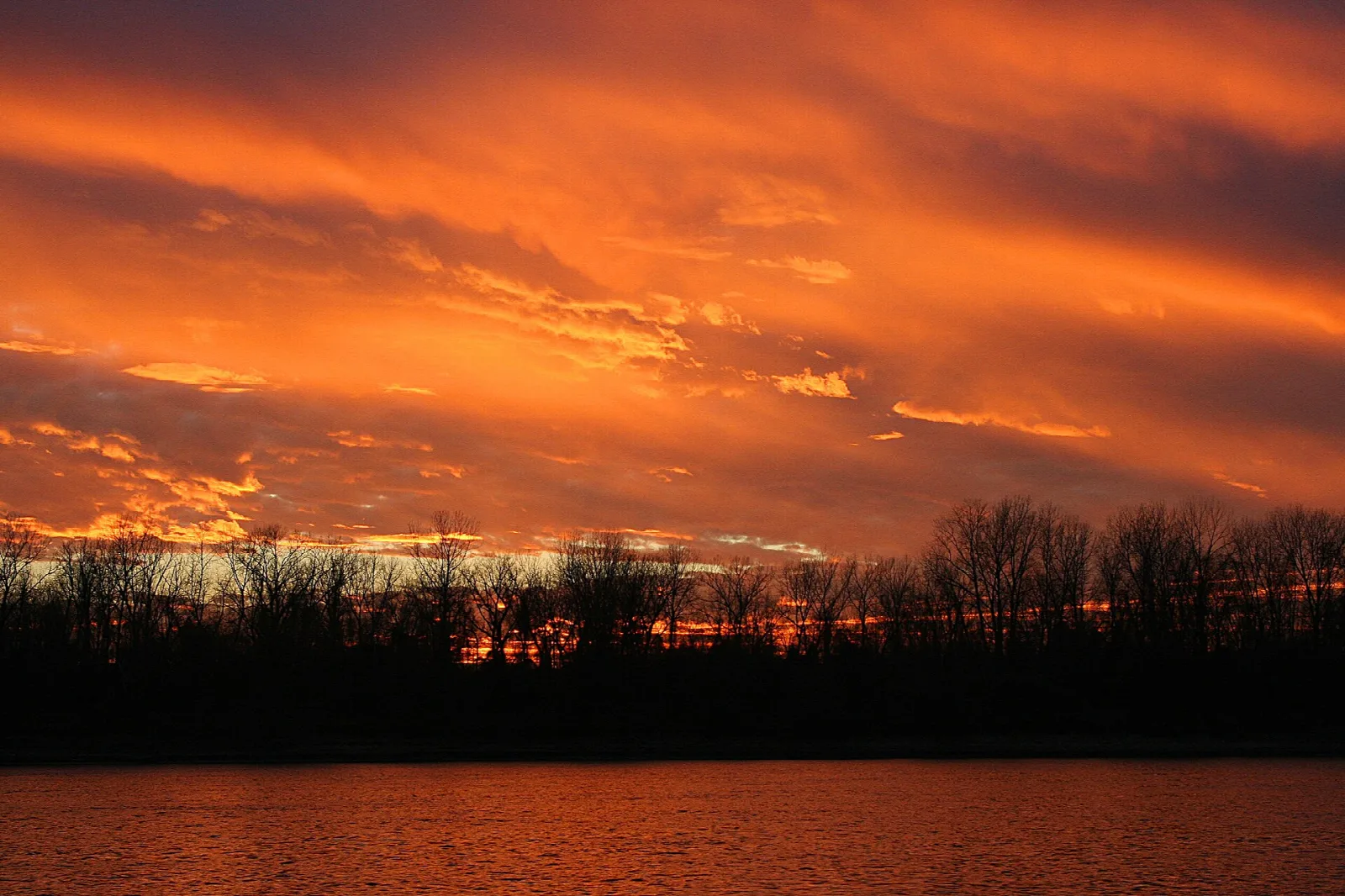 Orange and red sunset sky over dark trees and a river