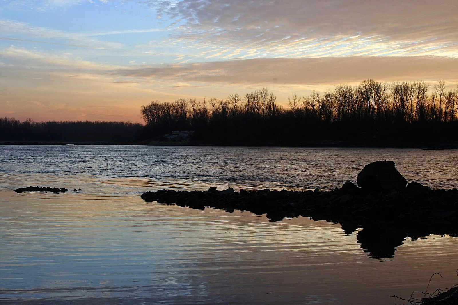 Rocky point jutting into calm water at dusk with bare trees on the far bank