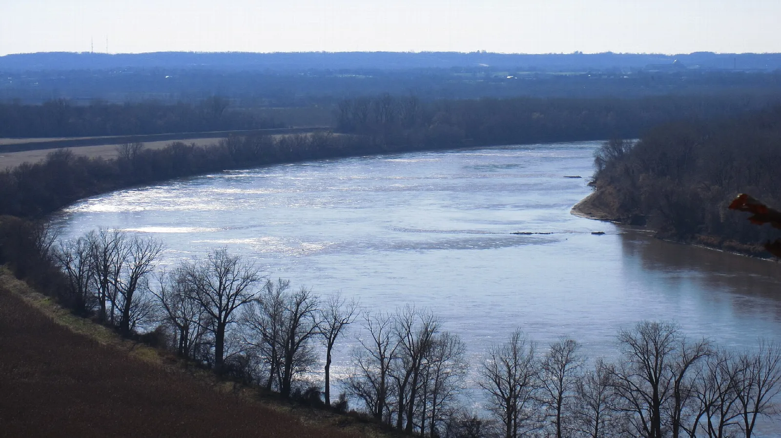 Wide river curving below a wooded bluff in winter
