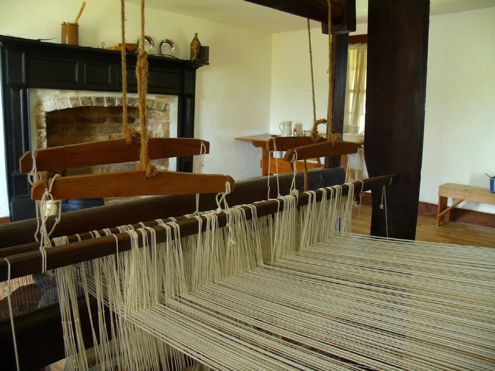 Wooden loom strung with white thread in a room with a fireplace