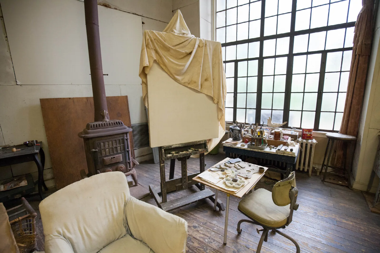 Artist studio with a large window, easel, wood stove and paint table