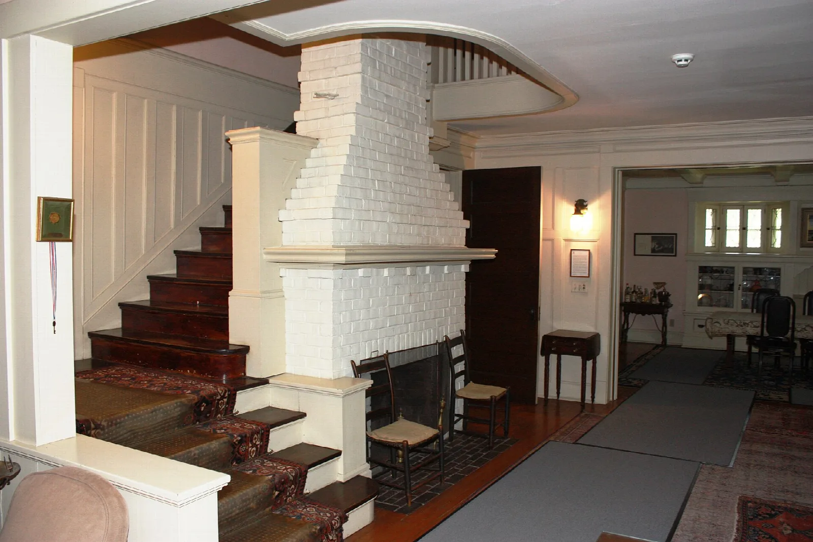 Entry hall with a red-carpeted staircase and white brick fireplace