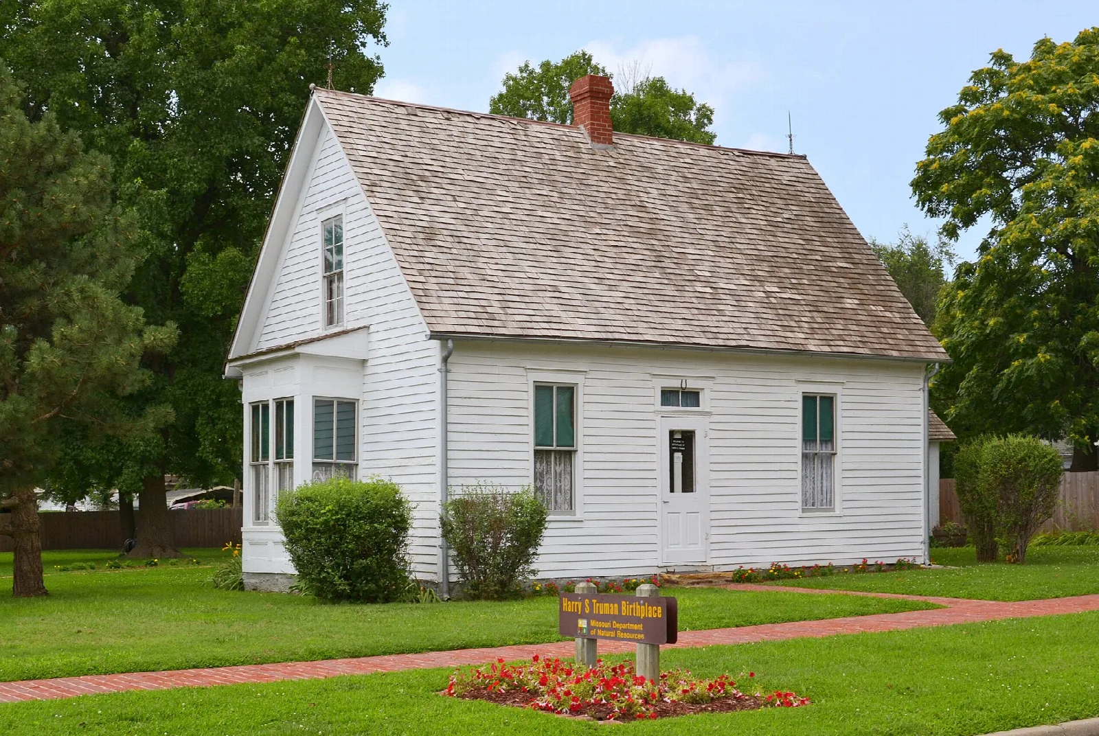 Small white house with a shingled roof, brick walkway and flower bed in front