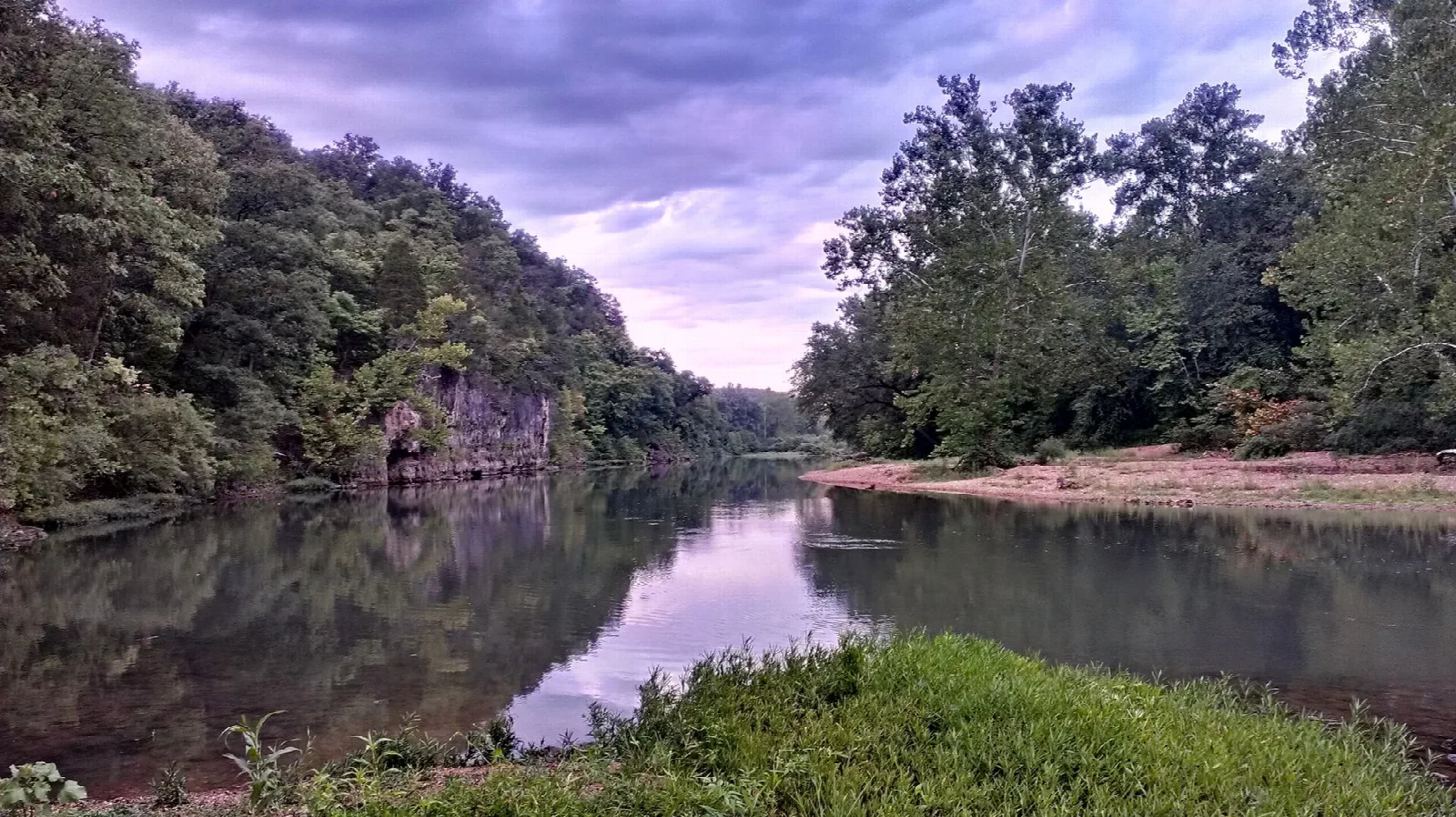 Calm river reflecting a purple sky between wooded banks and a rock bluff