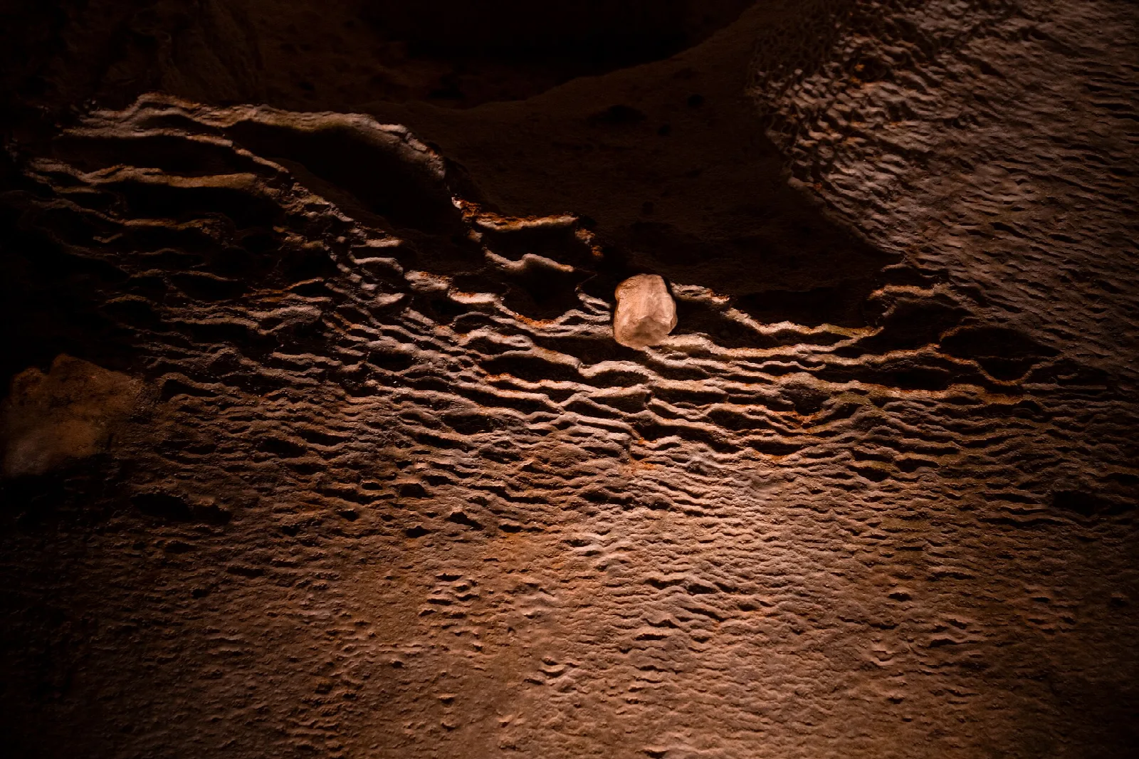 Rippled brown flowstone on a cave wall lit from the side