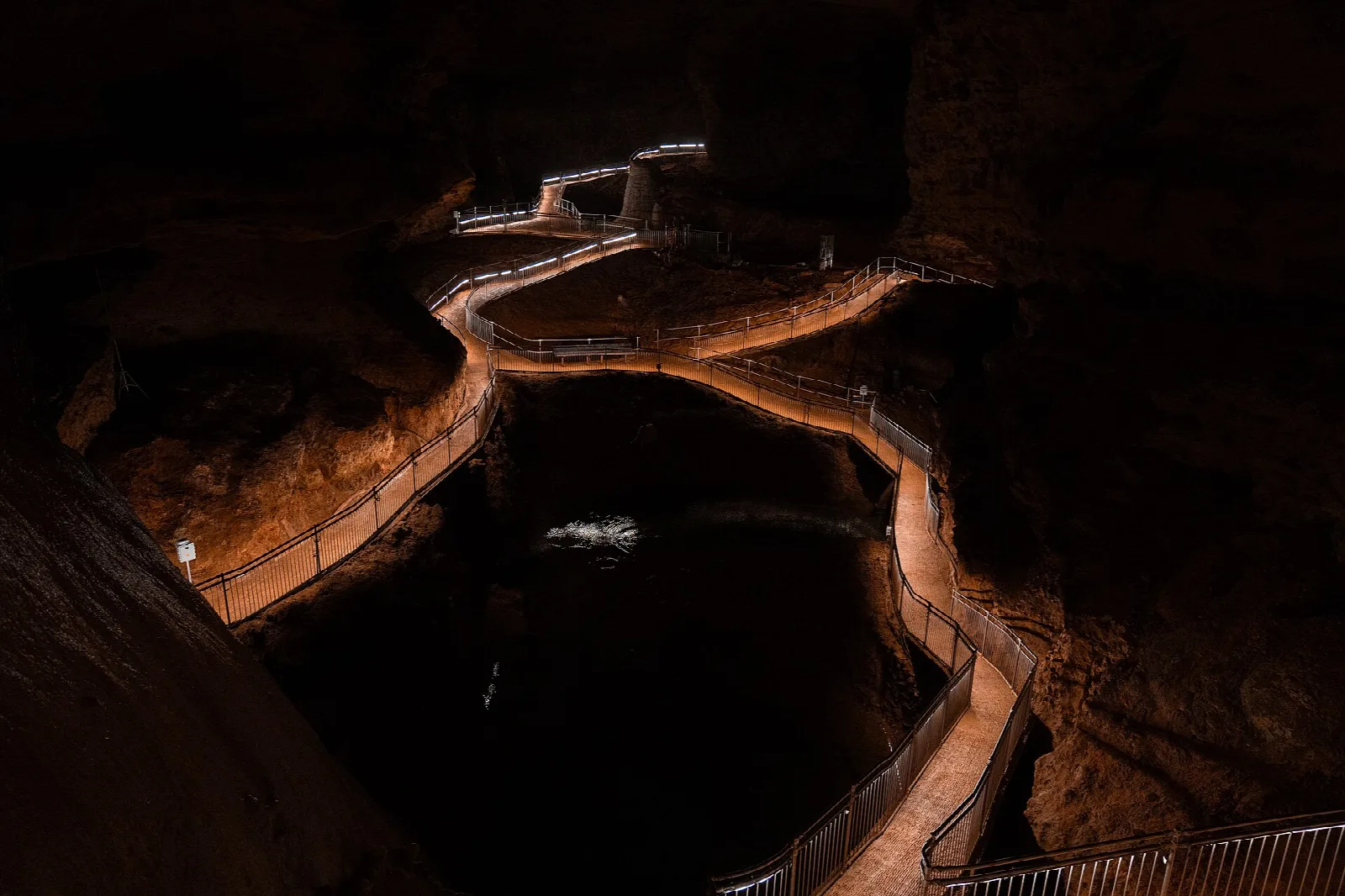 Lit walkway winding along a dark pool inside a cave