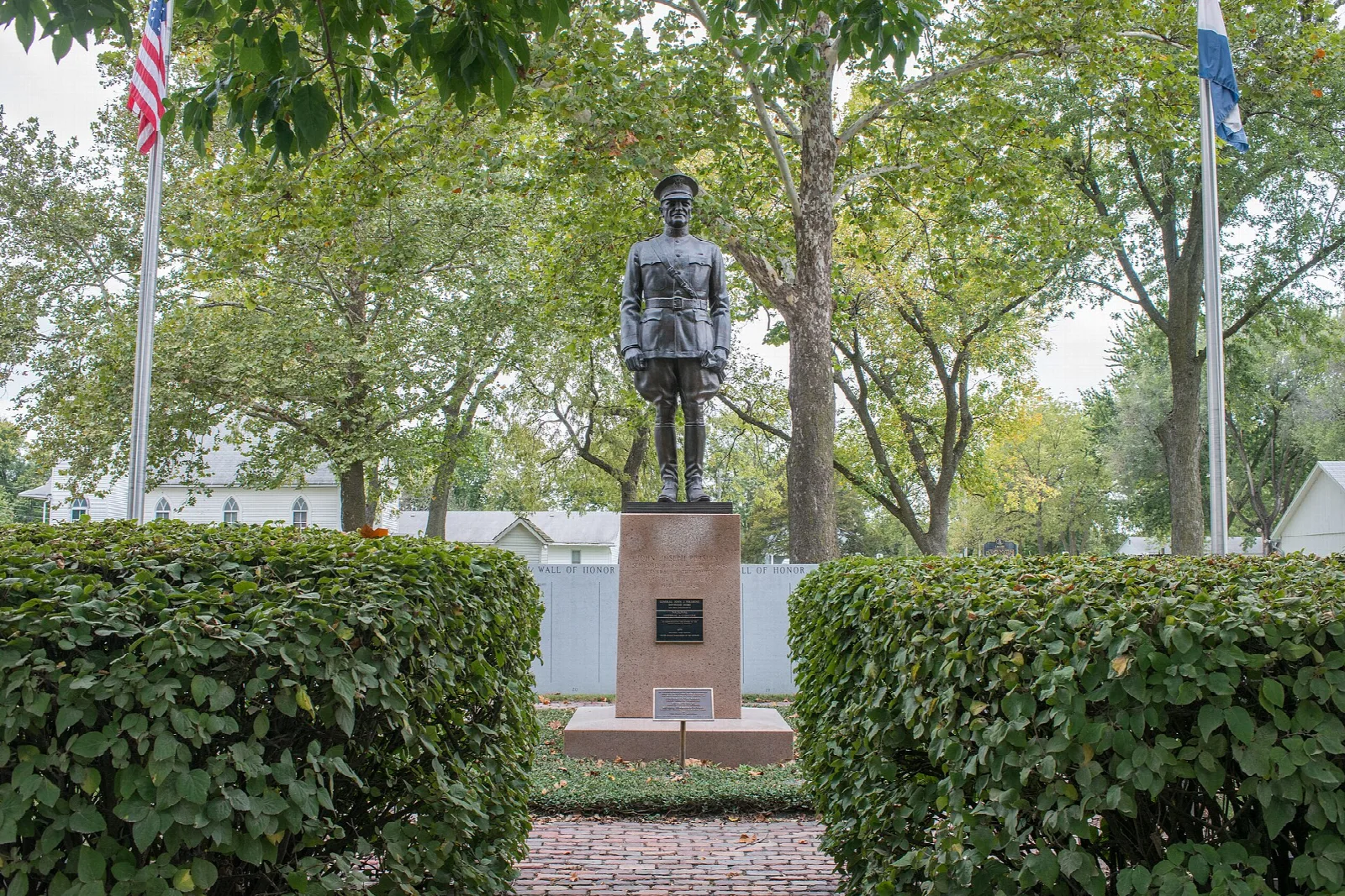 Bronze statue of a uniformed man on a stone base between hedges and flags