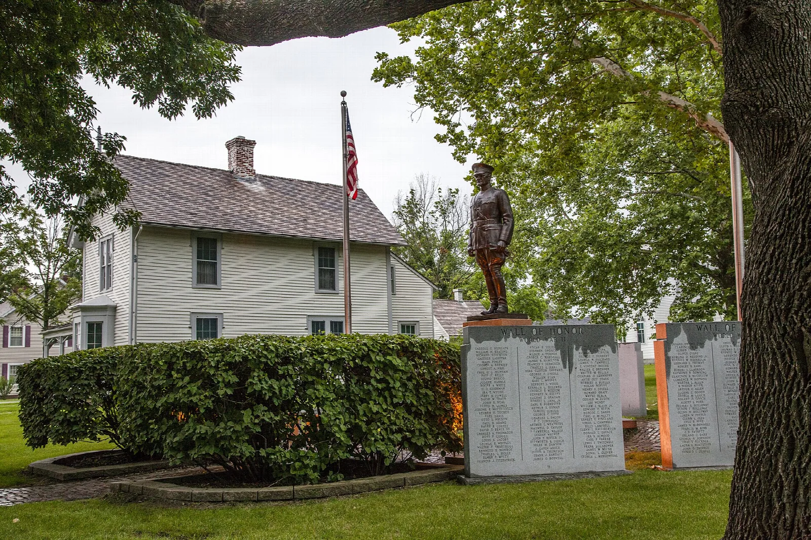 White house behind a flag pole and a statue, with stone memorial panels in front
