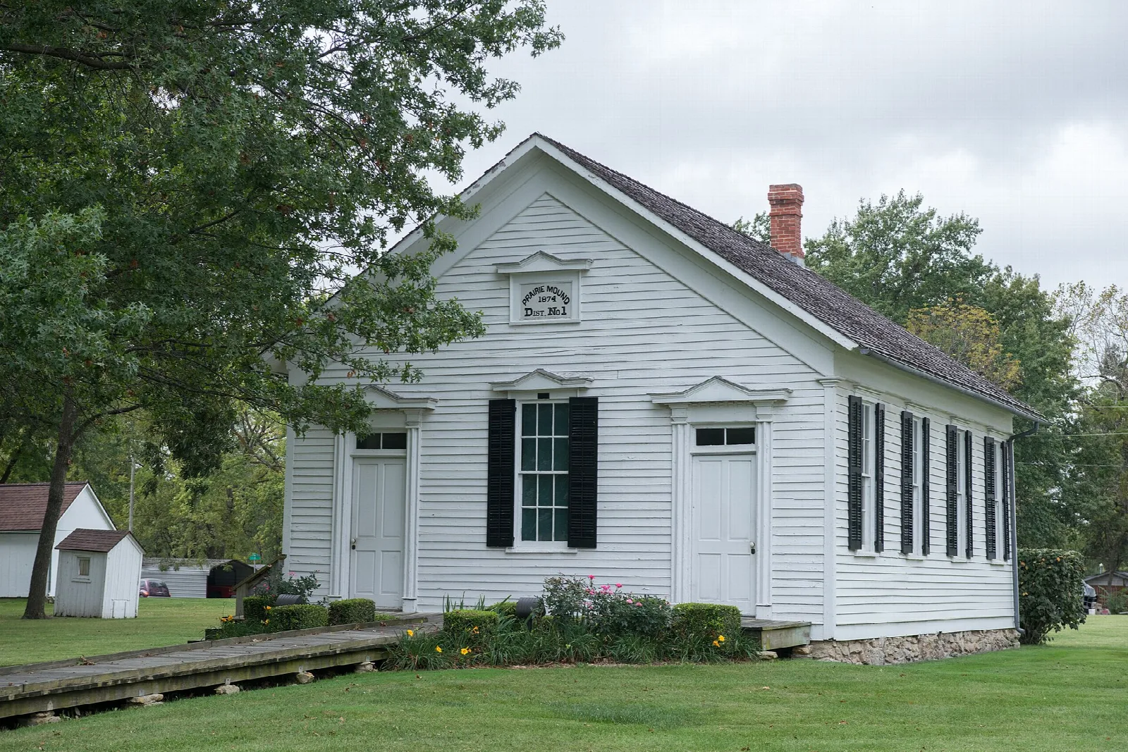 White one-room schoolhouse with a brick chimney among trees