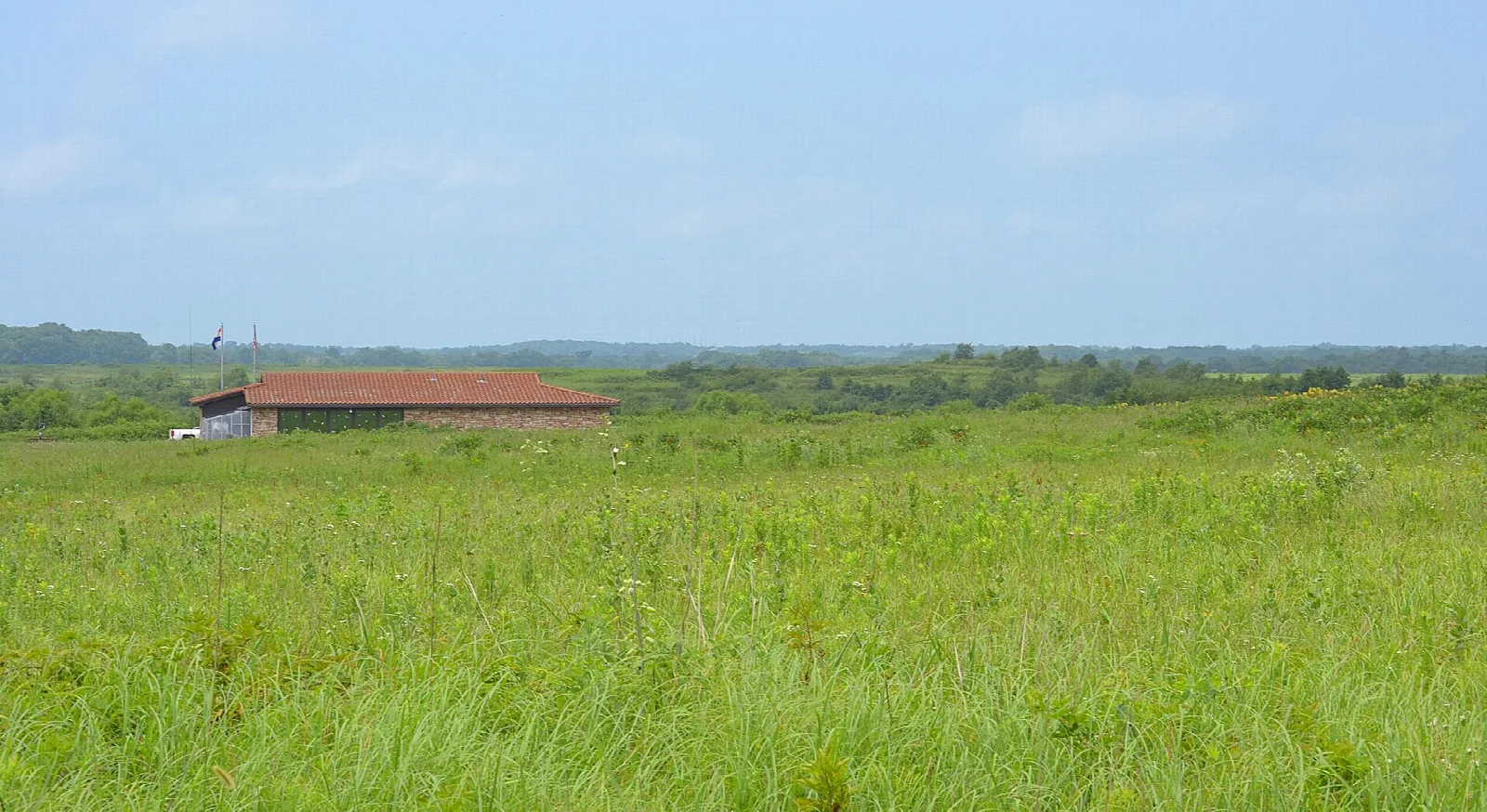 Low building with a red roof across a wide green prairie