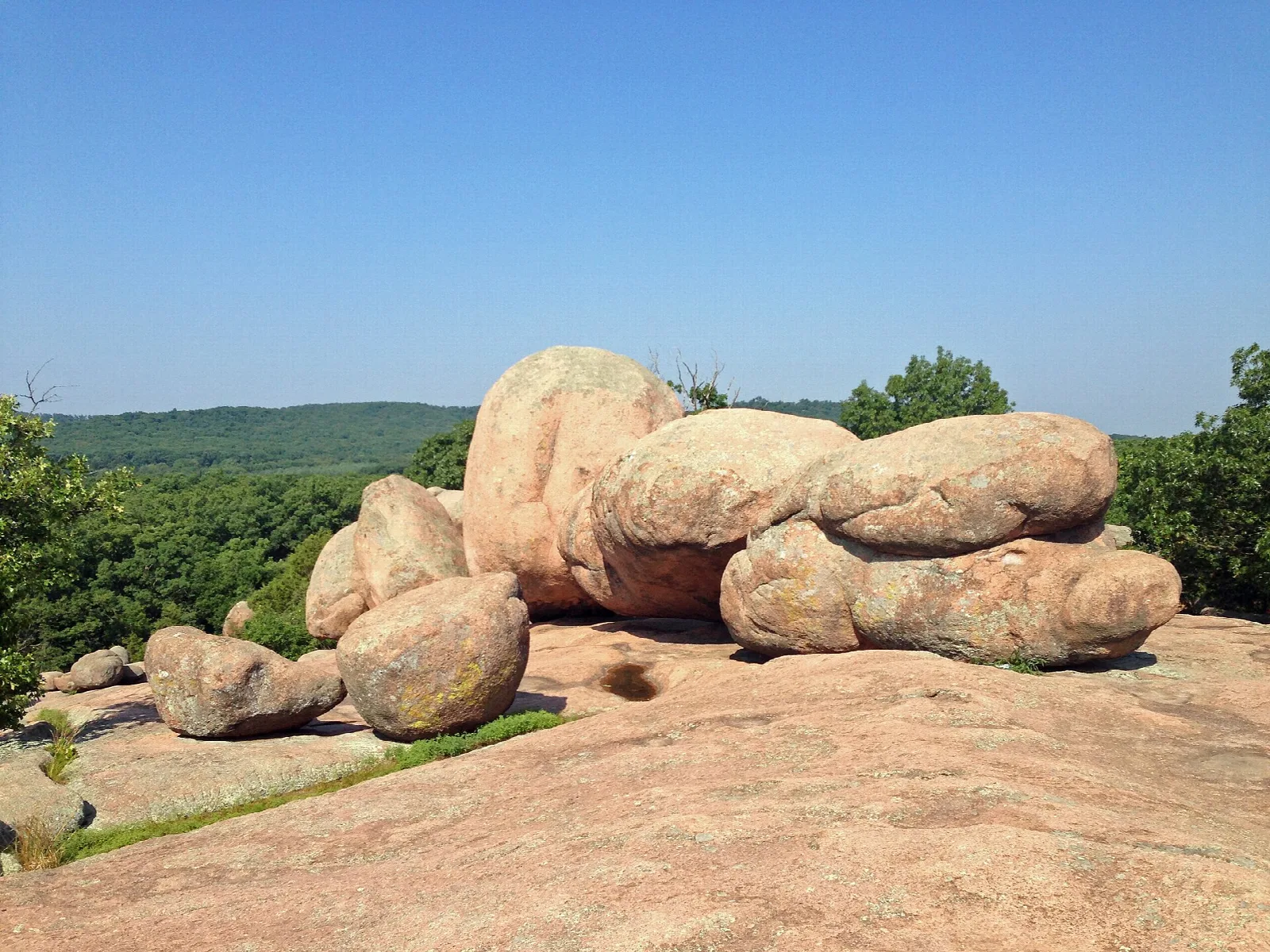 Large rounded pink granite boulders on a rock outcrop with forested hills behind