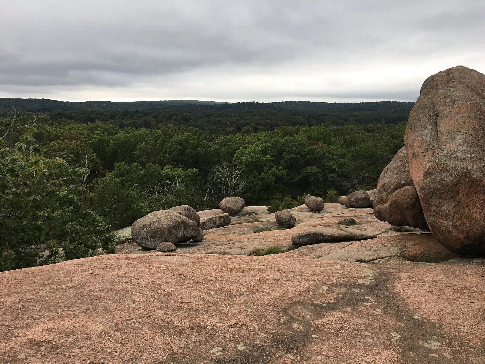 Granite boulders on a bare rock top above a wooded valley under cloudy sky