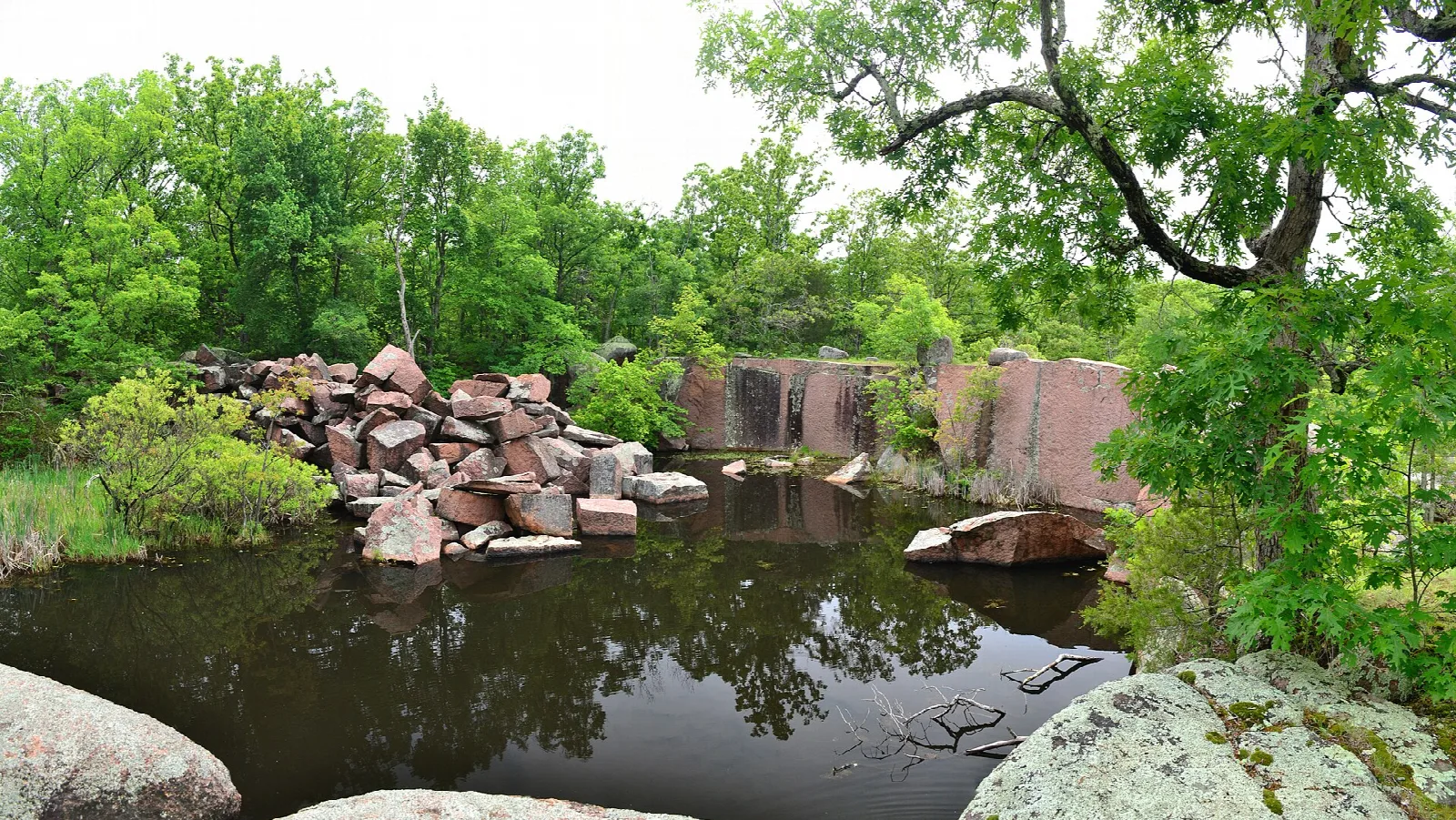 Quarry pond with piled granite blocks and green trees around it