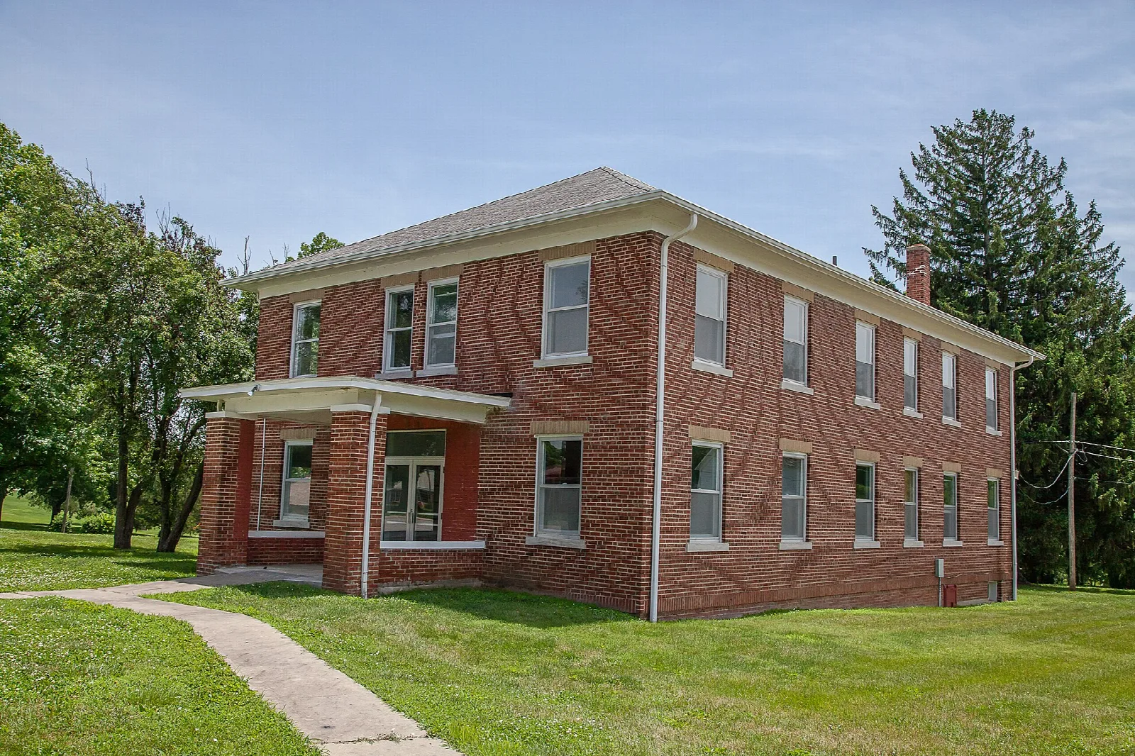 Two-story red brick building with a small porch and a sidewalk