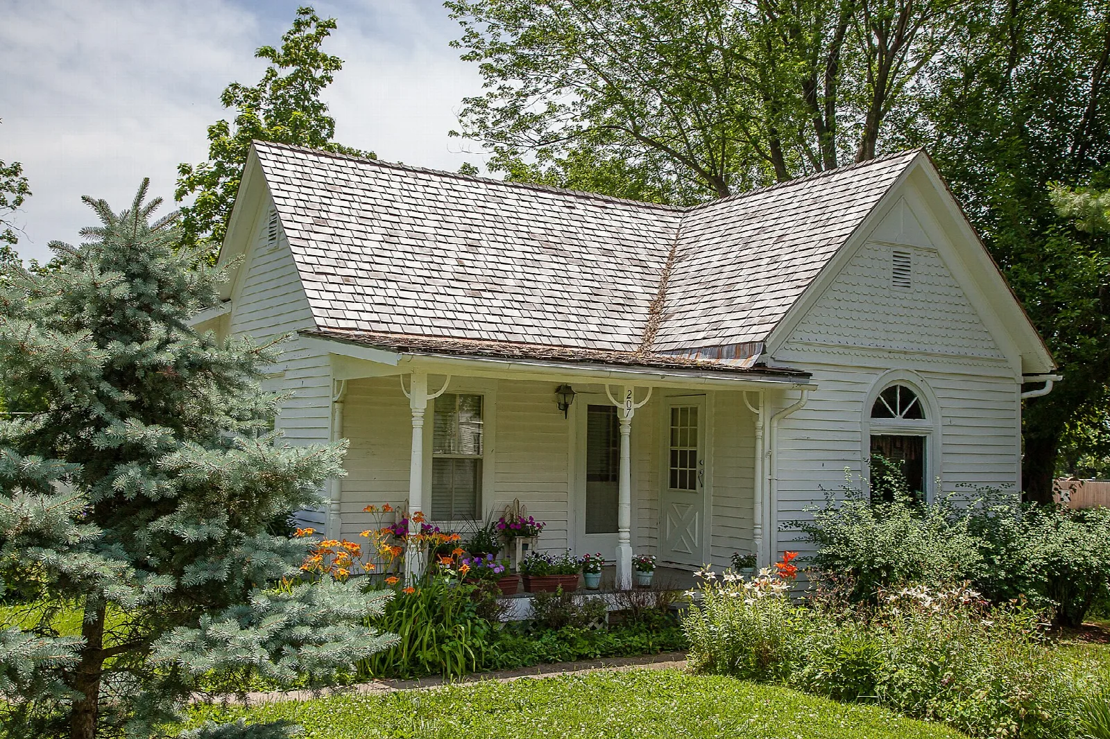 White cottage with a front porch and flower beds