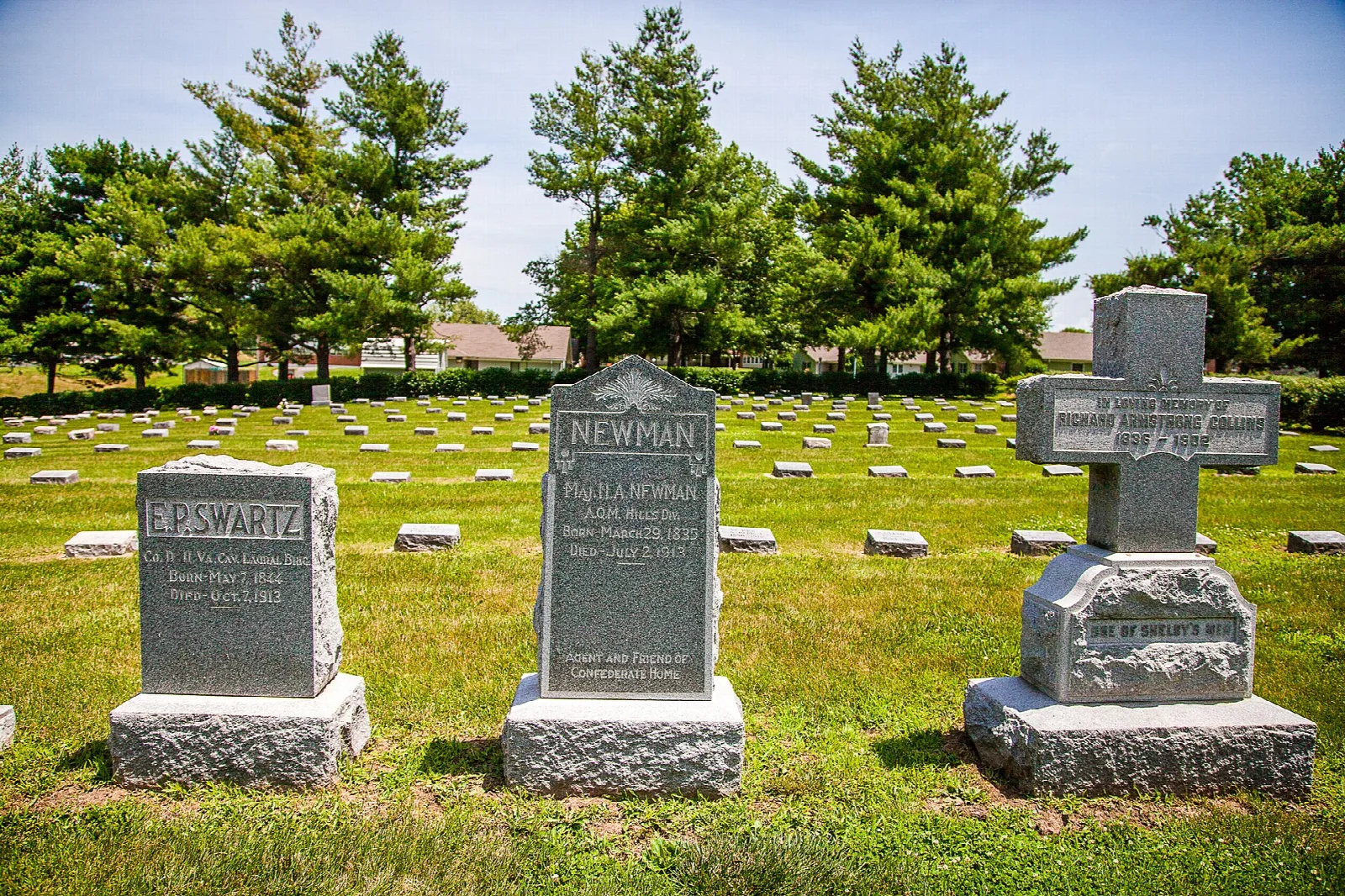 Rows of gravestones on a mown lawn with evergreen trees behind