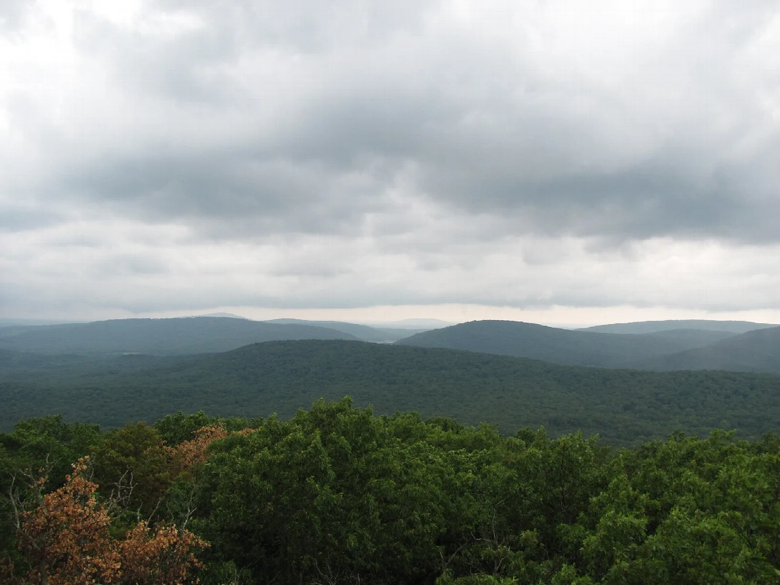 Wooded ridges stretching away under a cloudy sky, seen from a lookout with a bench