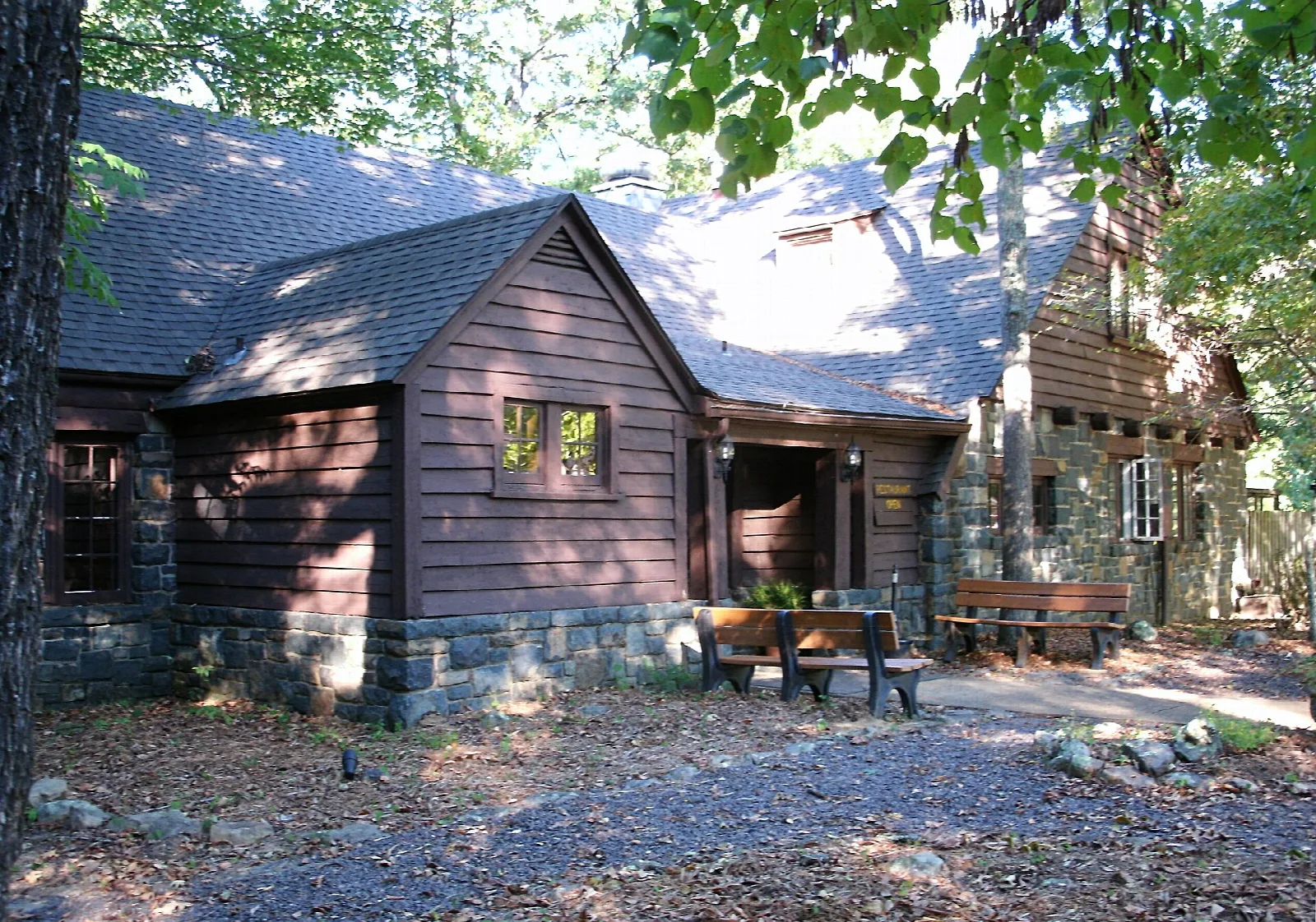 Stone and wood dining lodge among trees with benches out front