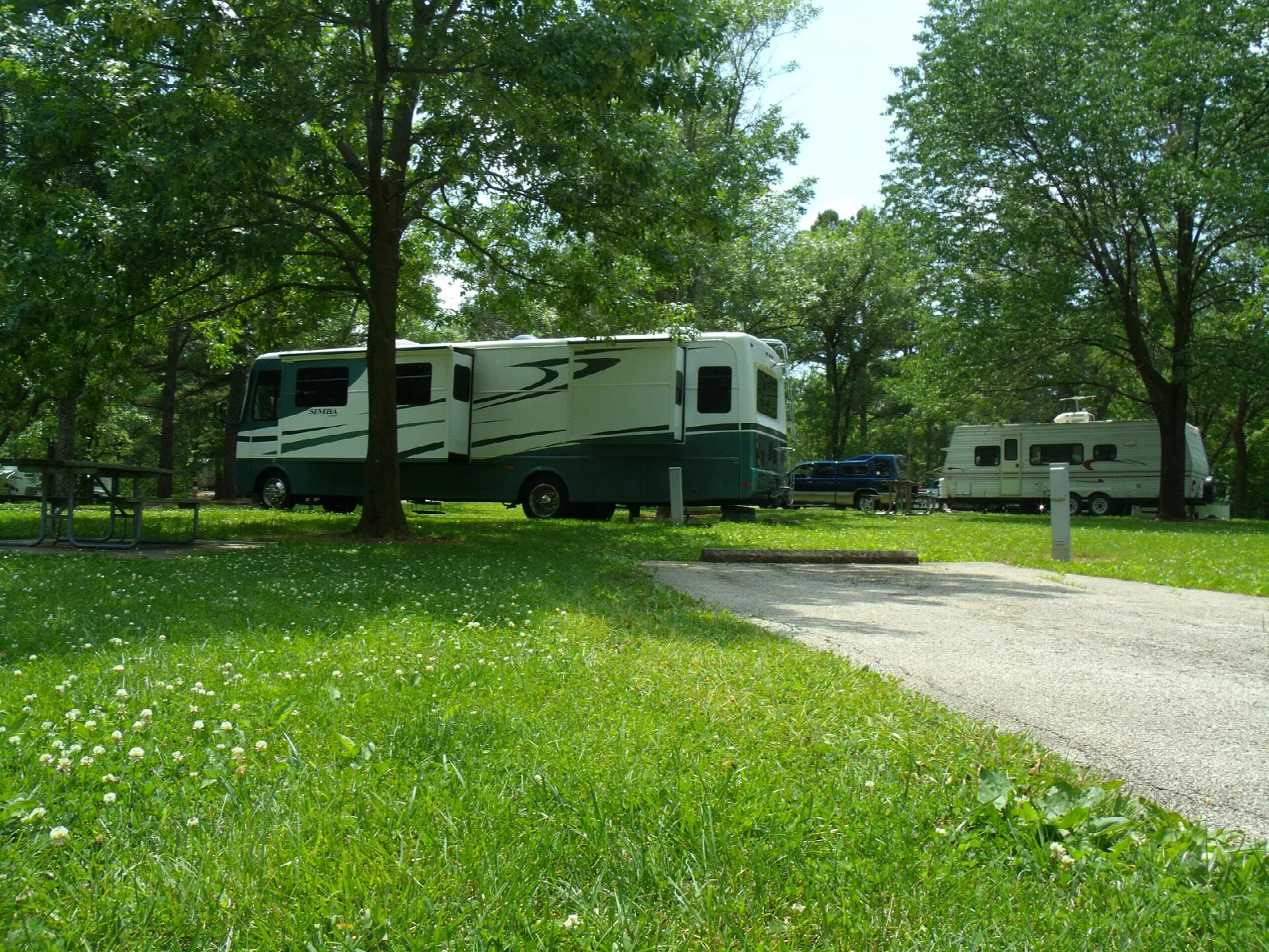 RVs parked on grass campsites under shade trees beside a paved loop