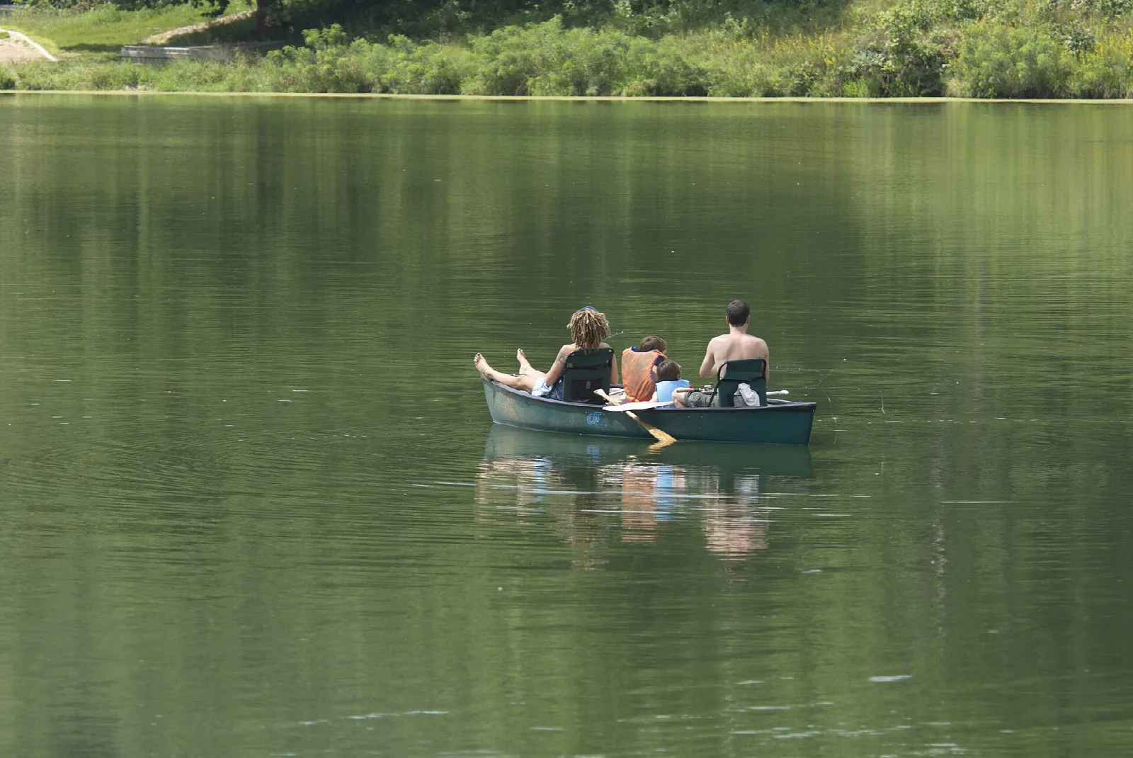 Three people in a rowboat on a calm green lake