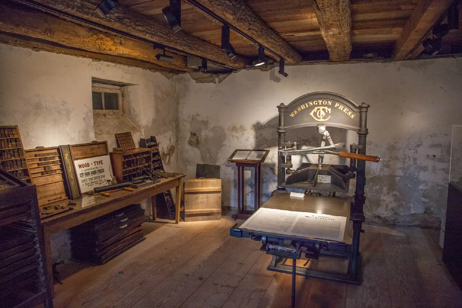Old wooden printing press in a stone-walled room with type cases