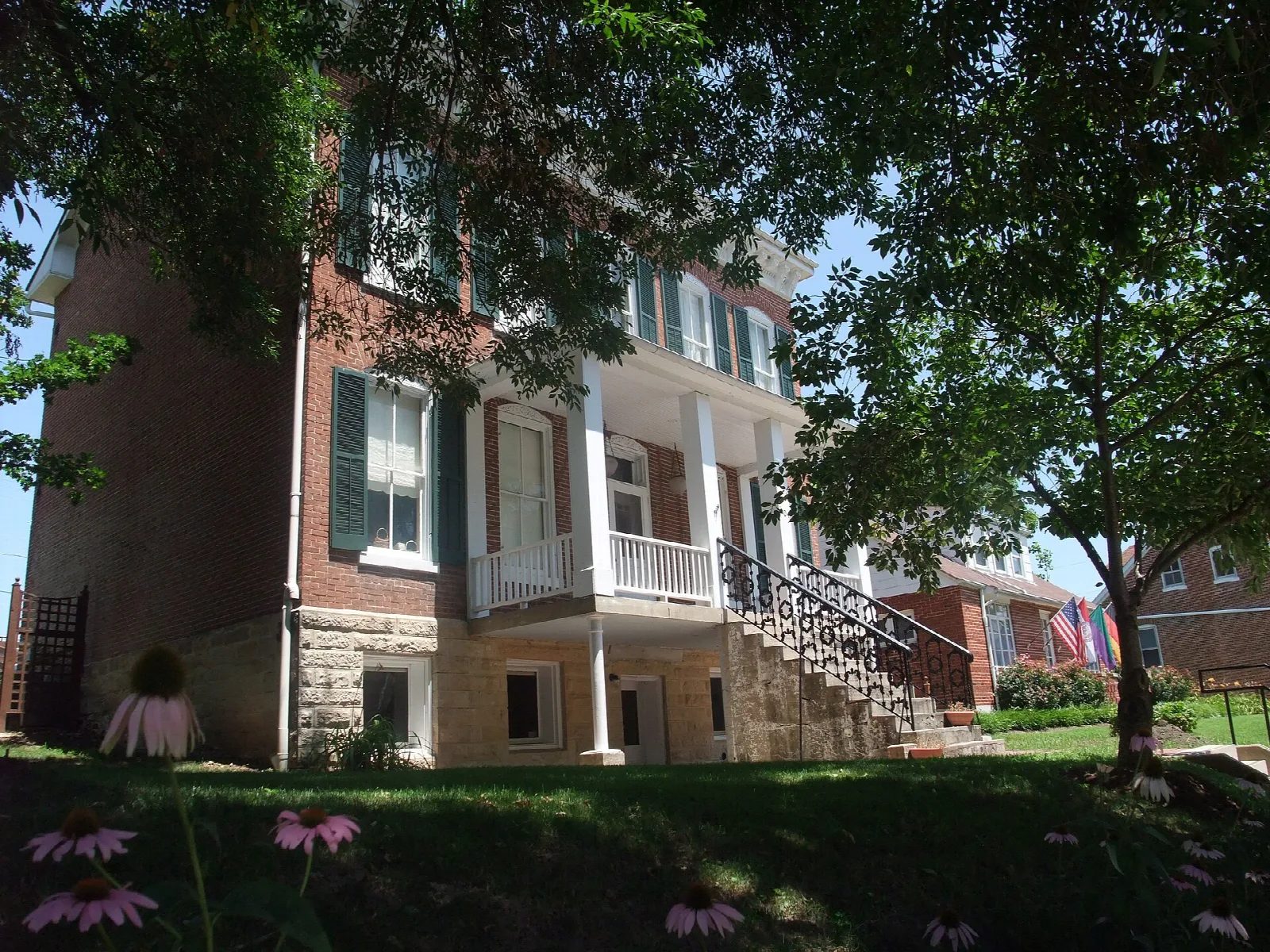 Brick house with a tall white-columned porch behind trees and flowers