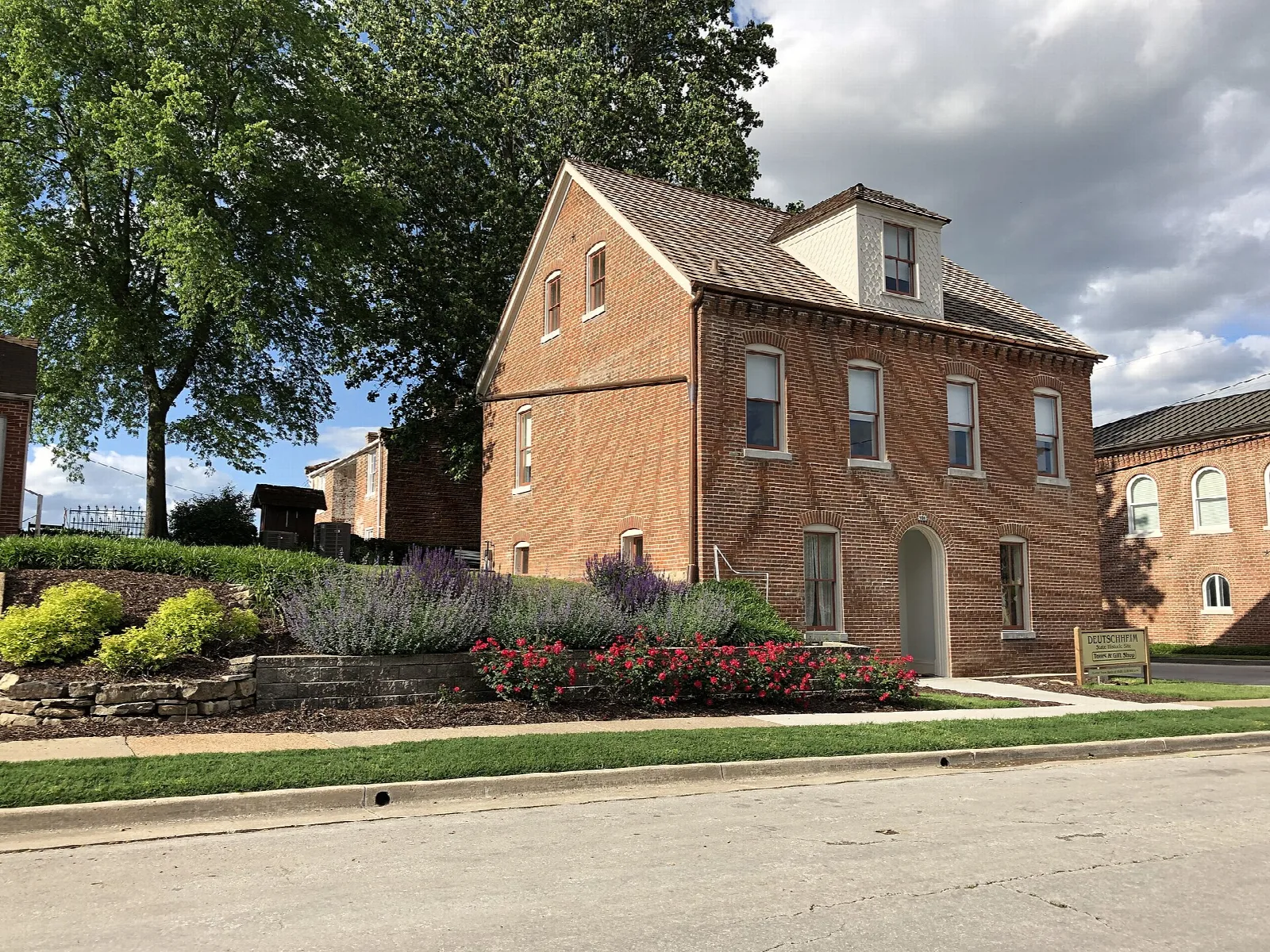 Brick house with a pitched roof seen from the street, with a flower garden in front