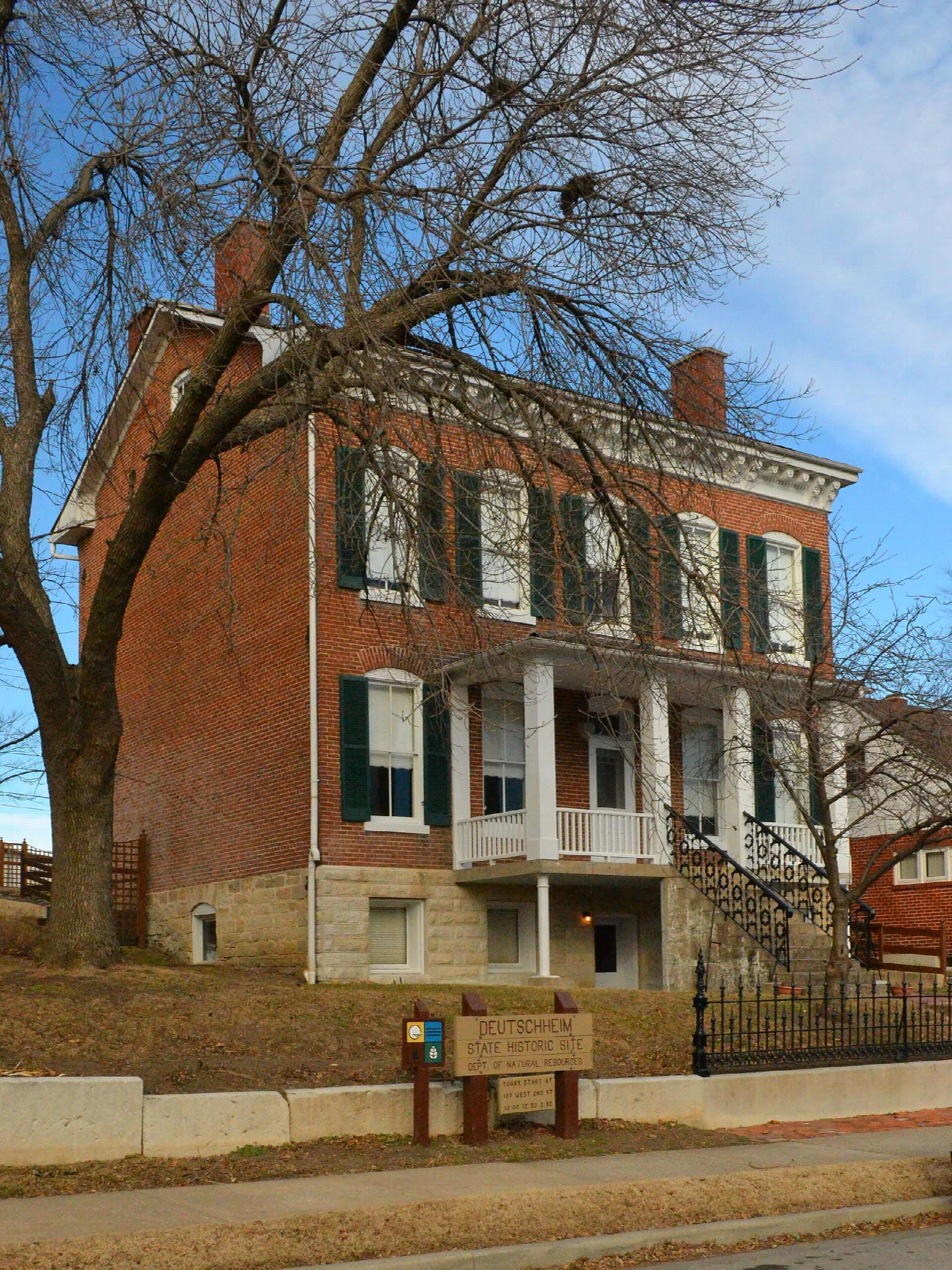 Red brick house with a two-level porch and a bare tree in front