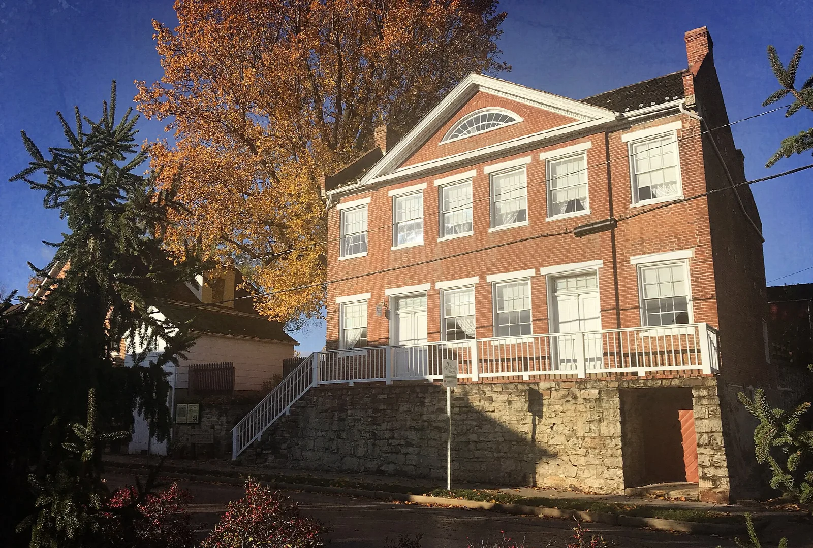 Two-story red brick house with a white porch and an autumn tree beside it