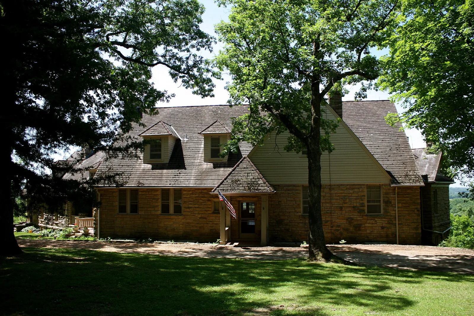 Low stone and stucco lodge with a gabled entry, set under large trees
