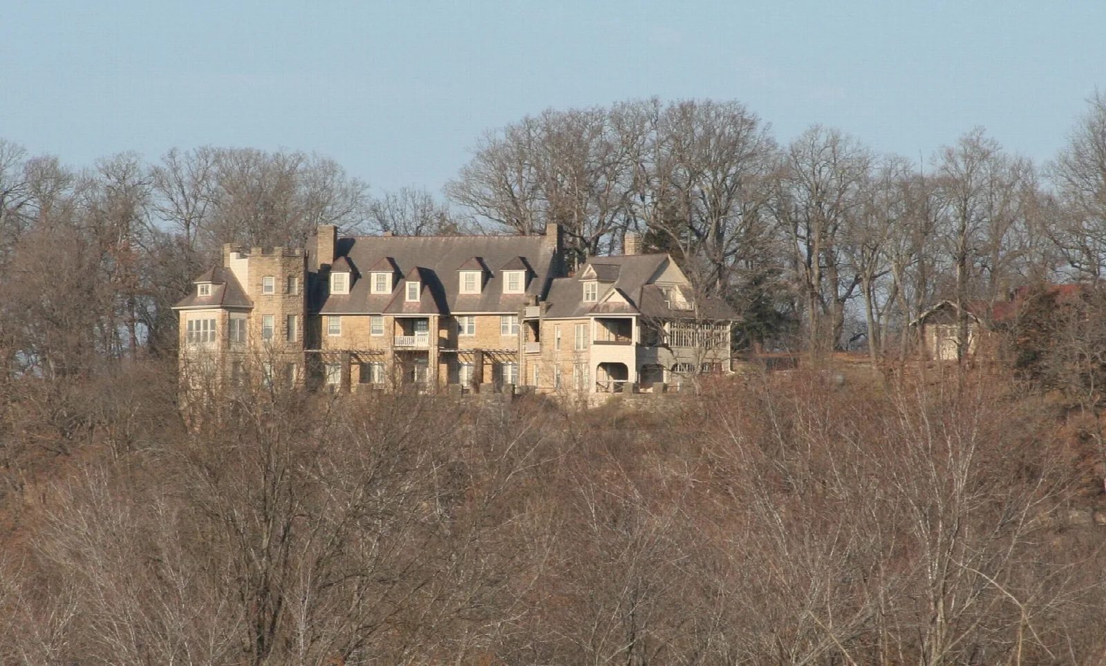 Stone lodge on a wooded hilltop seen from the valley below, with bare trees
