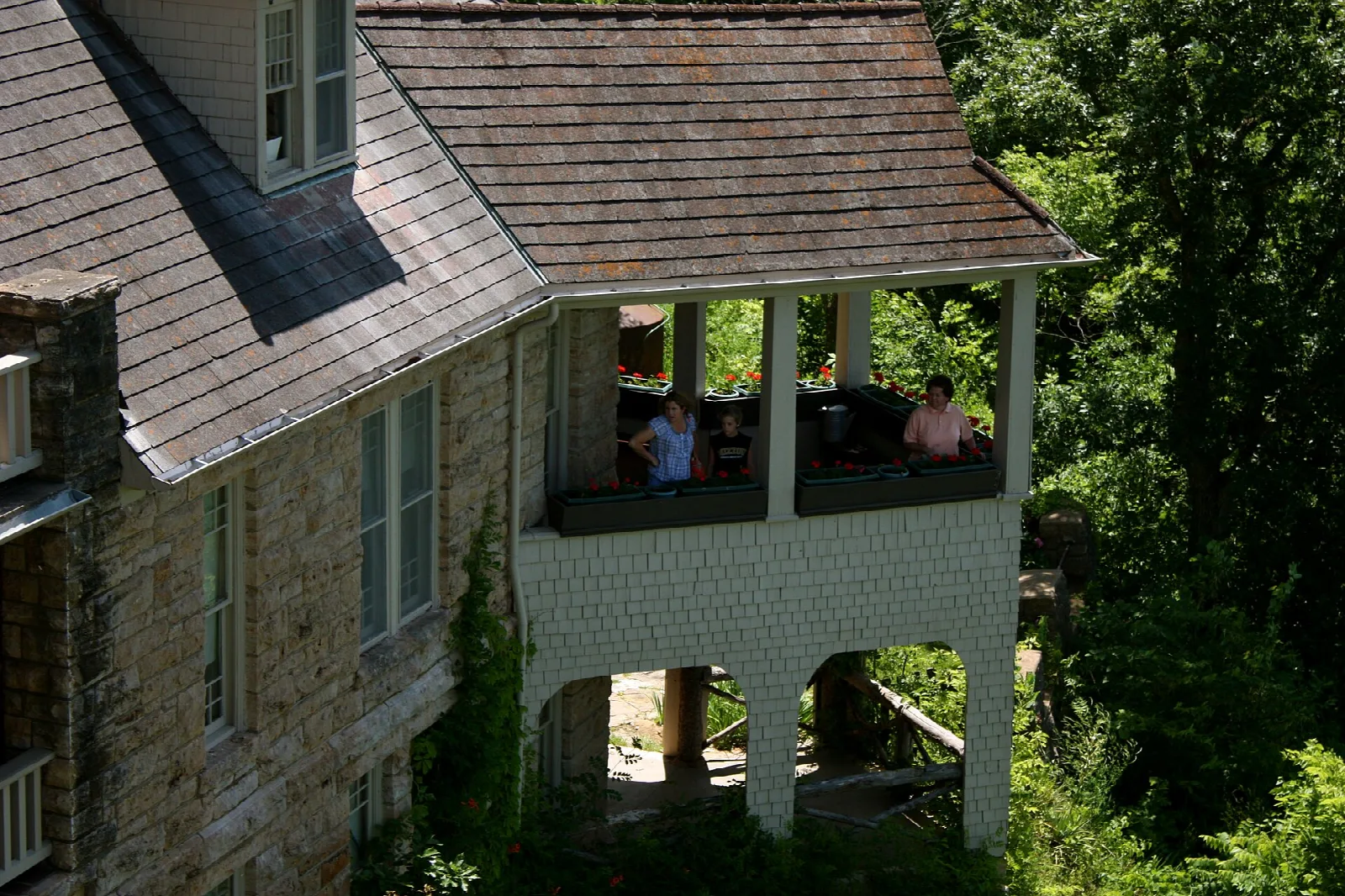 Stone lodge with a shingled roof and a covered porch beside green trees