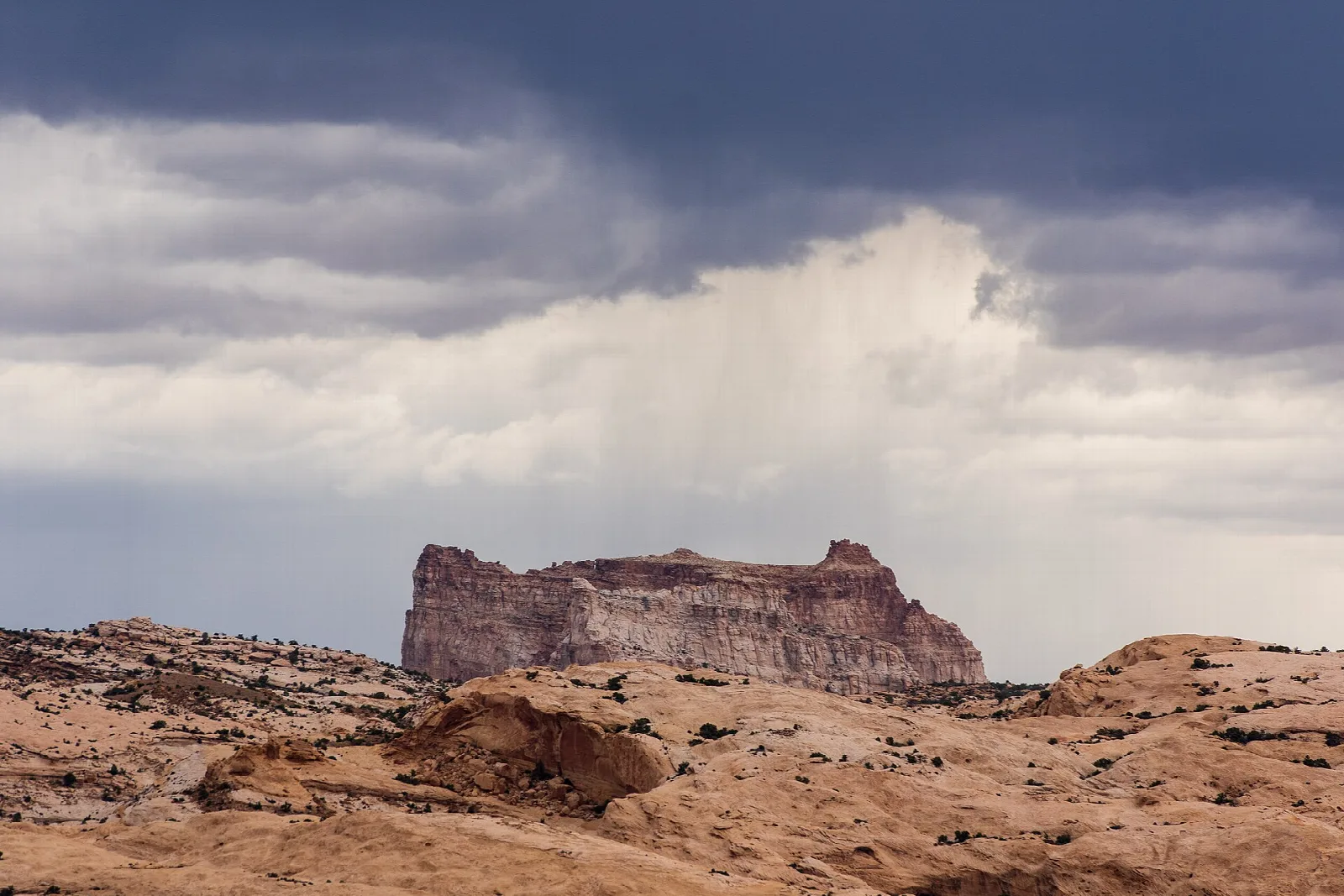 Distant flat-topped rock butte under a stormy sky with falling rain