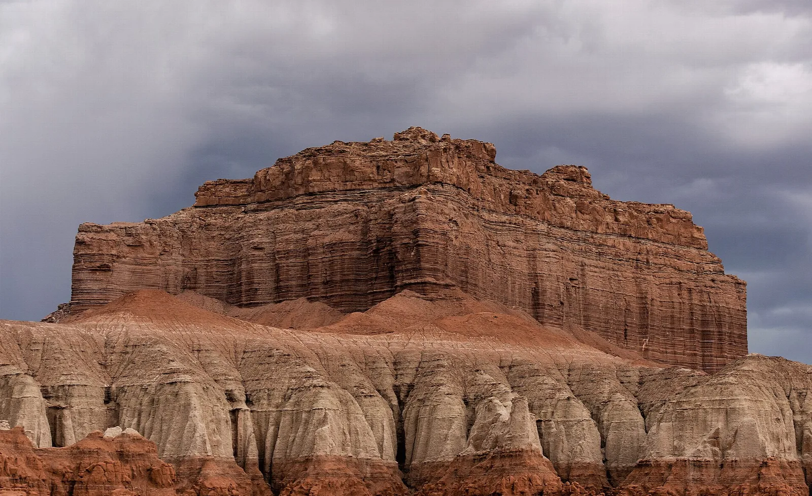 Layered cliff of a tall butte rising above gray and tan banded slopes
