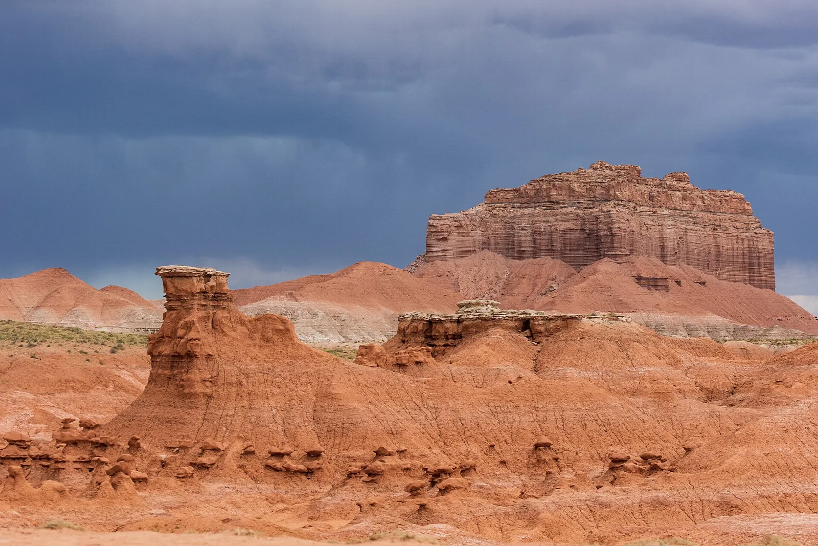 Weathered red rock goblins in front of a layered butte under dark clouds