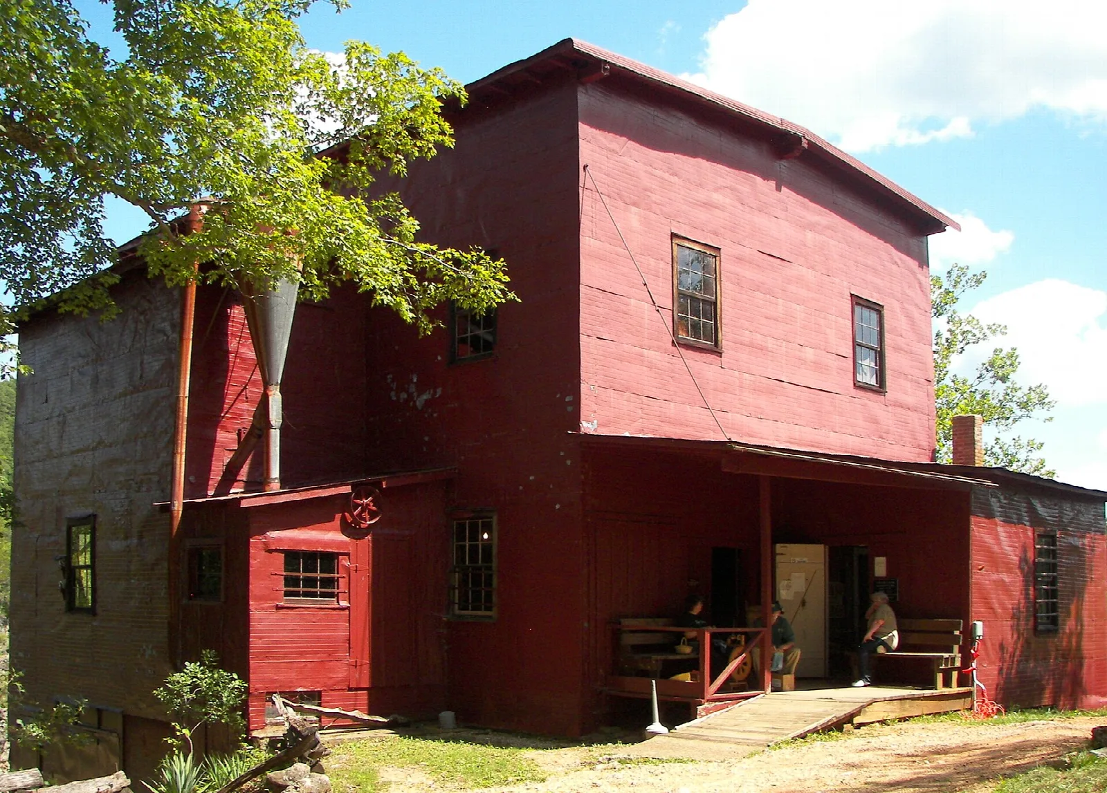Red wooden mill building with a porch and trees beside it