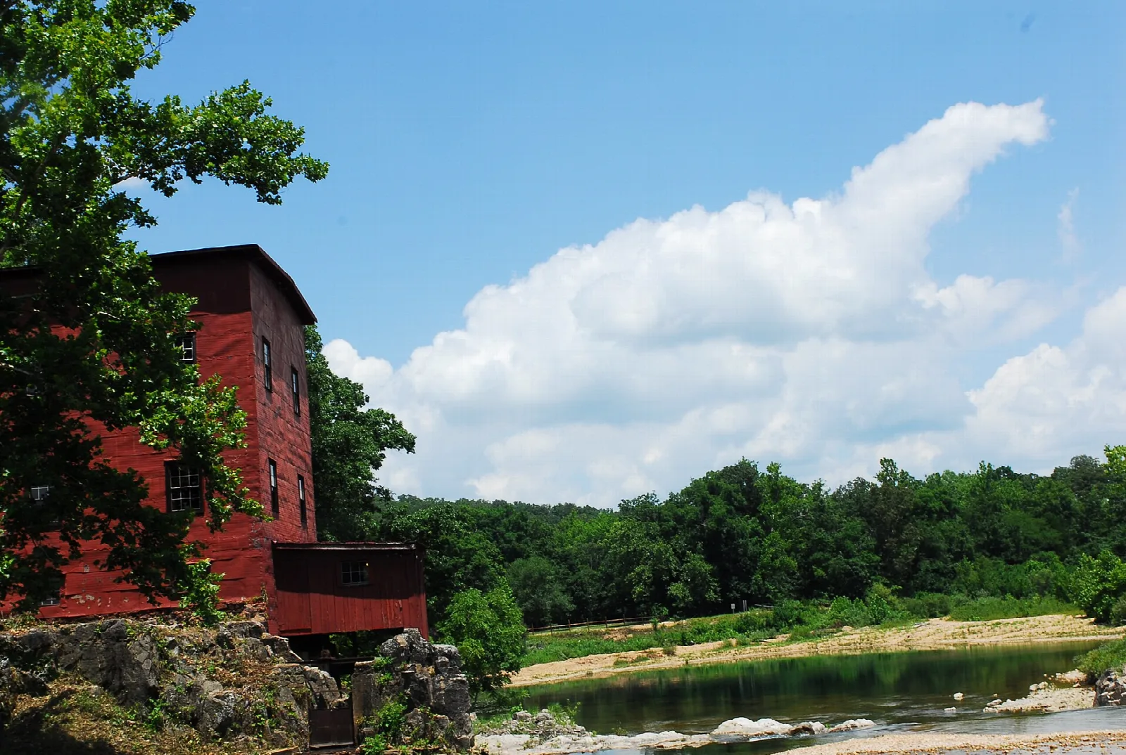 Red mill wall on a rocky bank above a creek and tree-lined shore