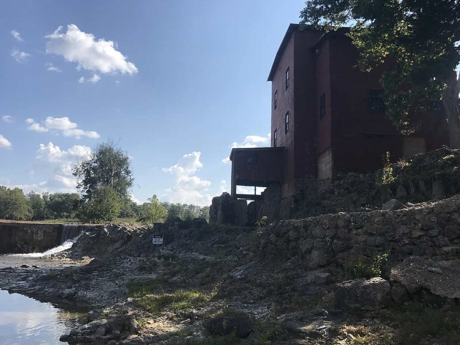 Tall dark mill beside the creek and a stone wall under a blue sky