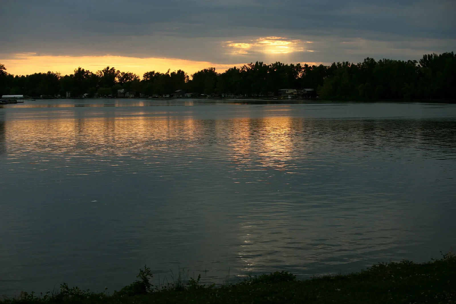 Lake at sunset with a glowing orange sky and a dark tree line