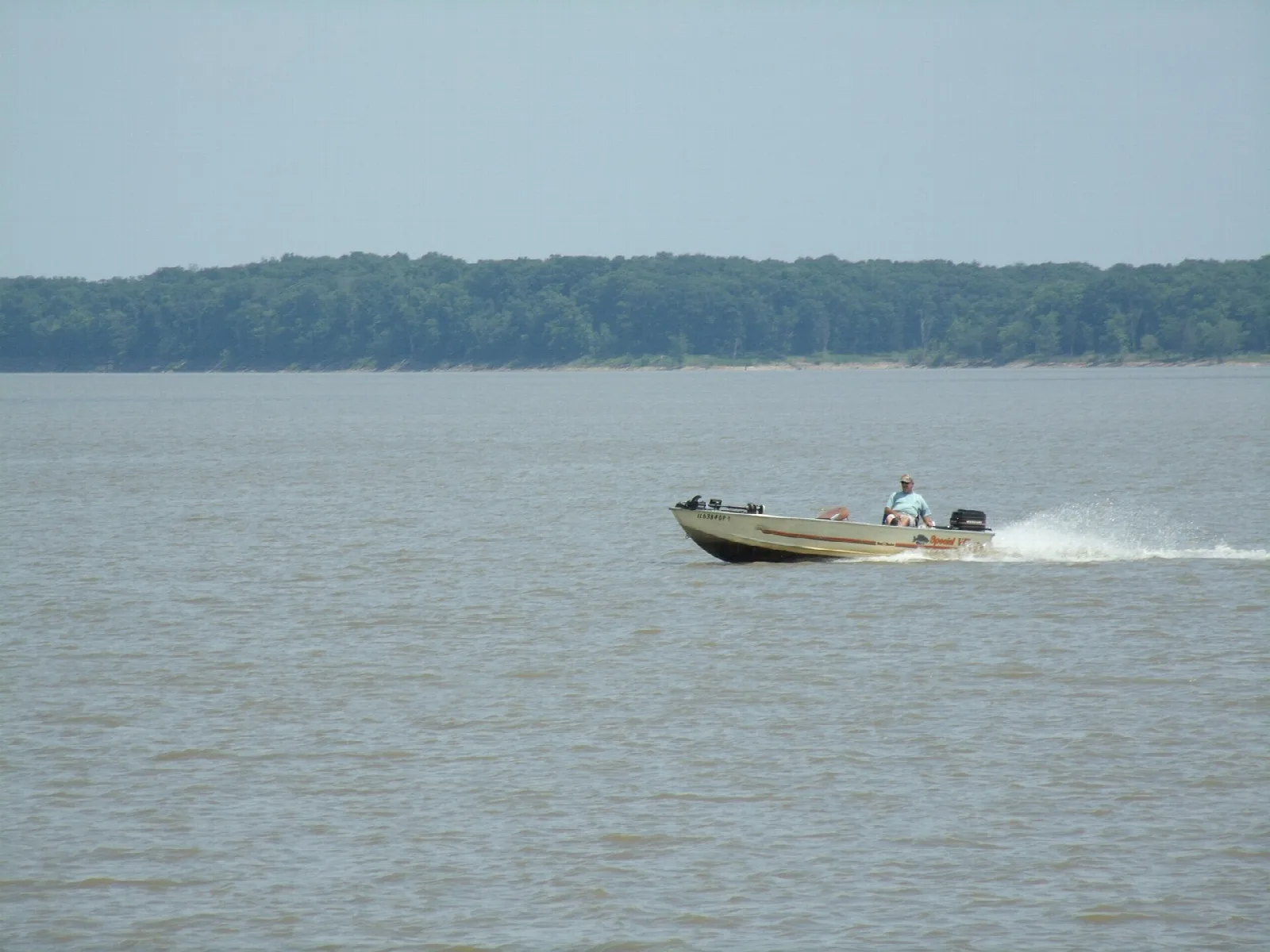 Motorboat crossing a wide lake with a tree-covered far shore