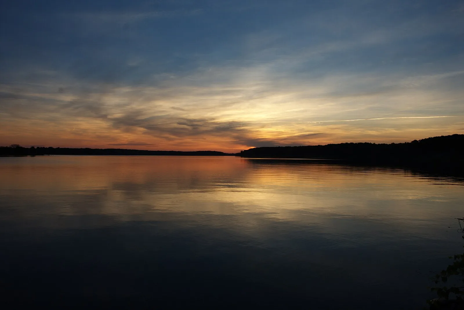 Lake at dusk with an orange and blue sky over a dark shoreline