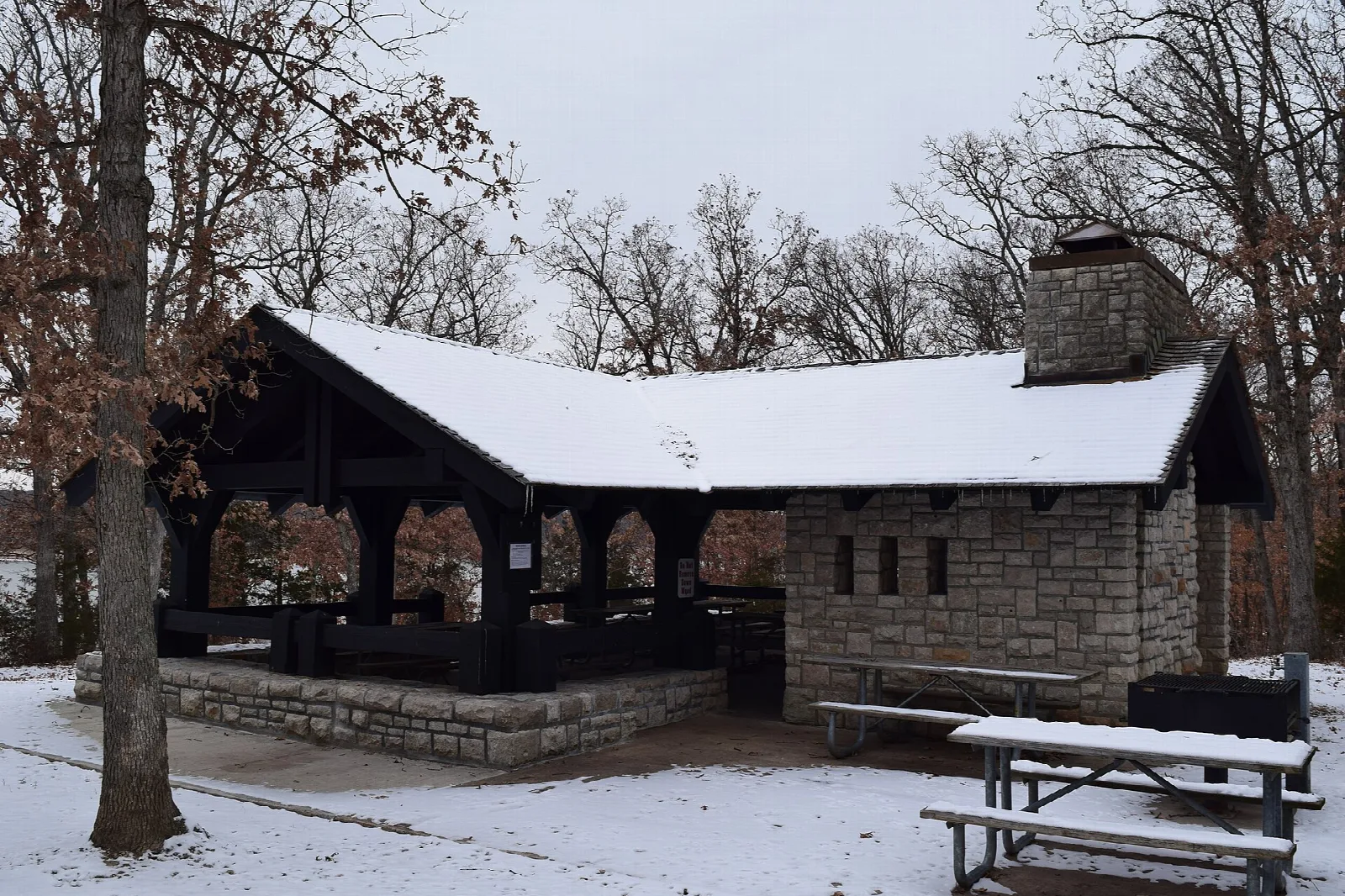 Stone picnic shelter dusted with snow among bare trees