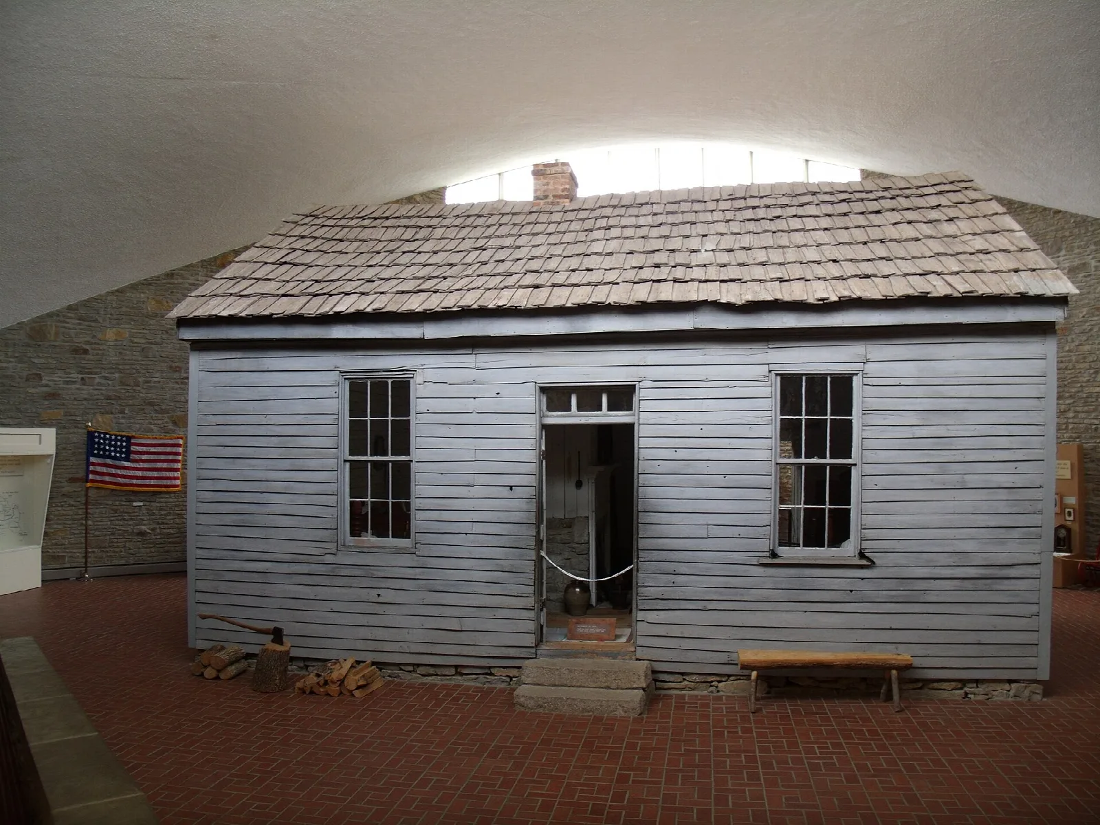 Gray wooden cabin with an American flag, displayed under a curved roof