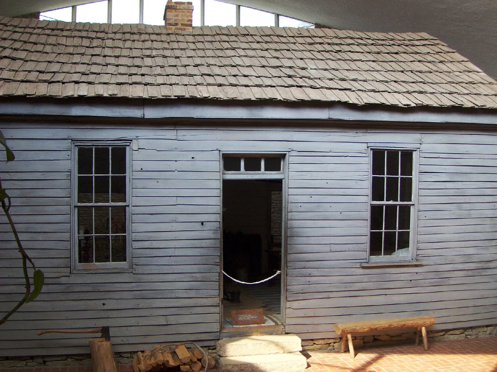 Small gray wooden cabin with a shingled roof, open doorway and two windows