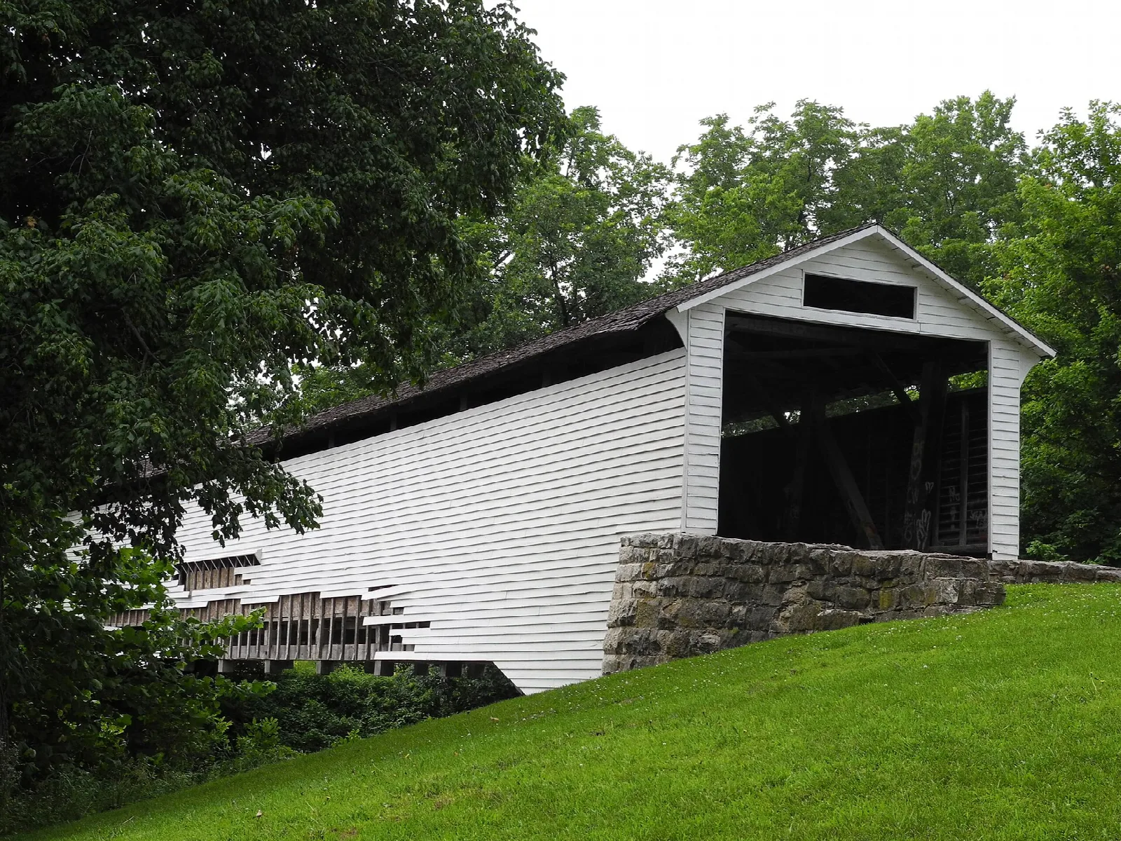 White covered bridge on a stone base beside a green lawn and trees